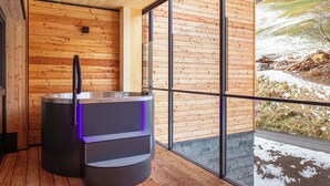 Una sauna con interior de madera y vistas a un paisaje nevado a través de grandes ventanales.