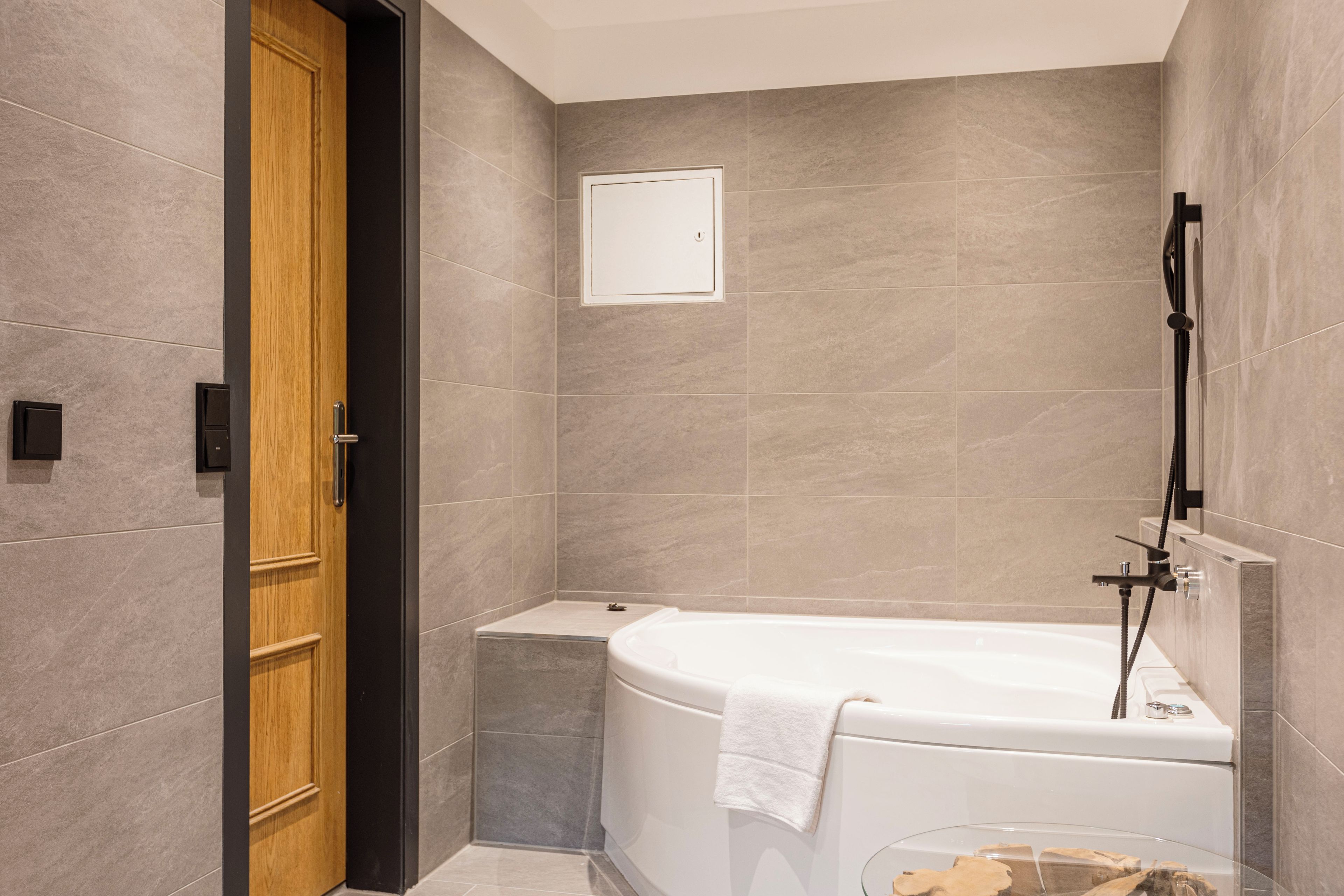 Ein modernes Badezimmer mit einer Badewanne, einer Holztür und einem kleinen Glasbehälter.