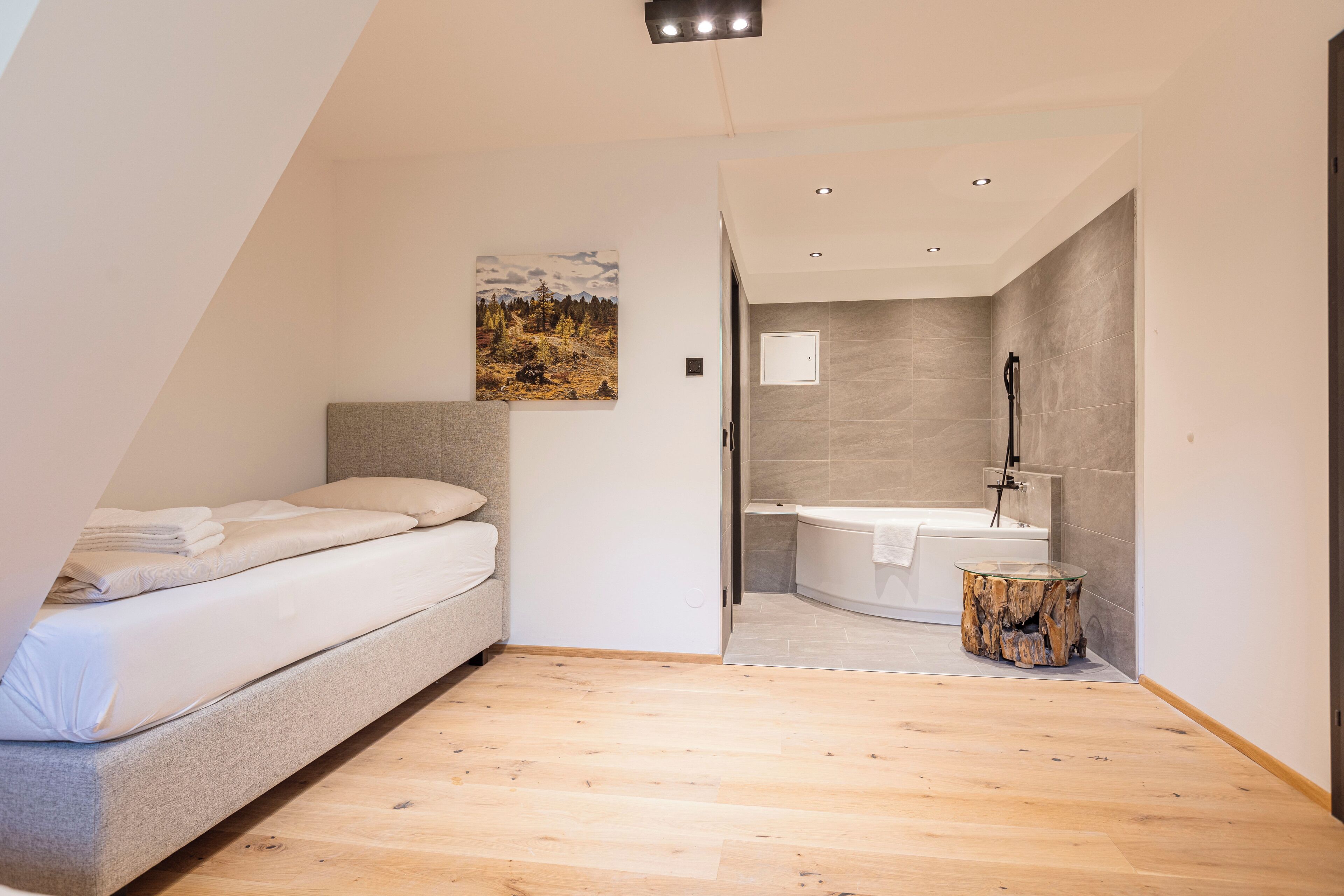 Un dormitorio moderno con cama, un cuadro y baño con bañera y lavamanos.