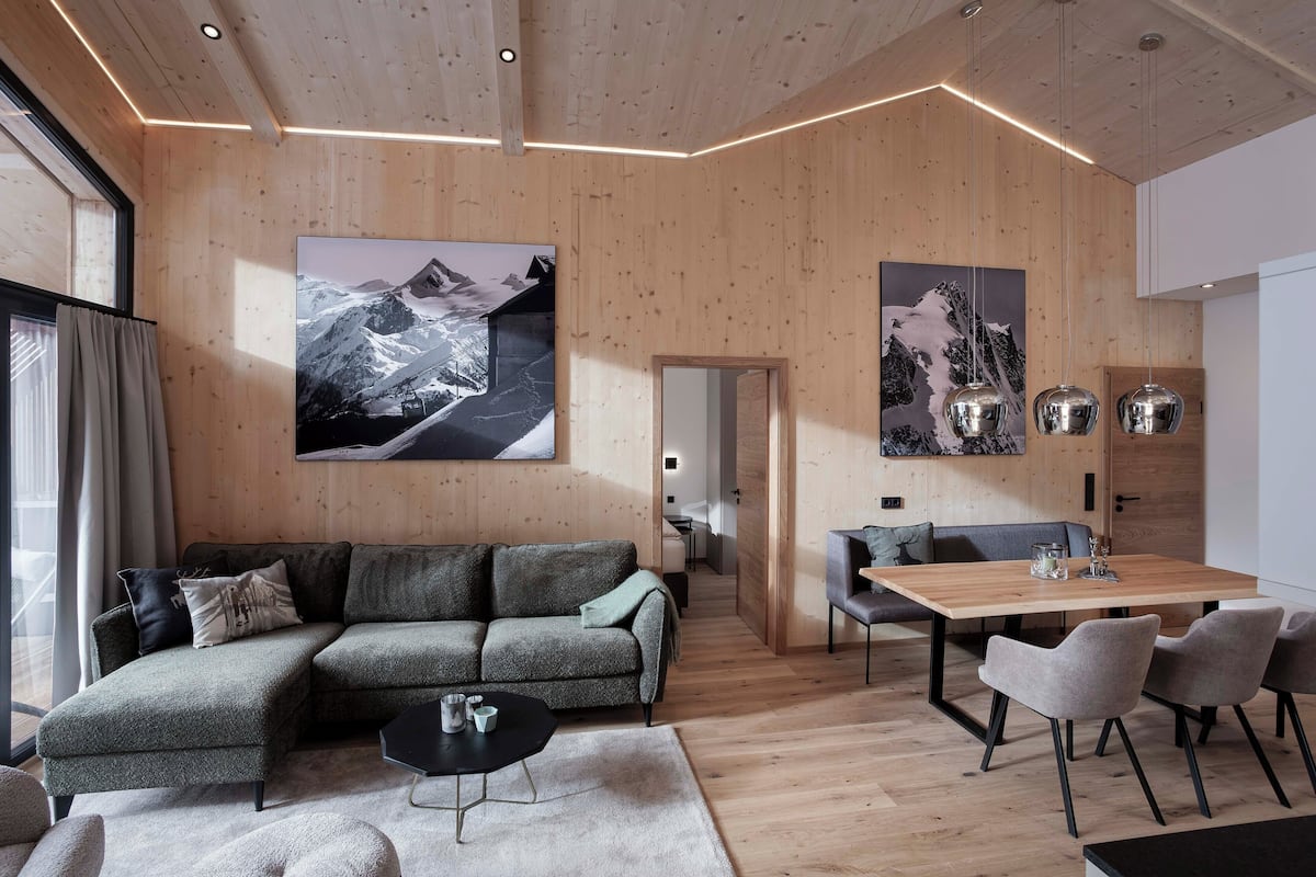 Ein modernes Wohnzimmer mit Holzboden und -wänden, einem Ecksofa, einem Esstisch mit Stühlen und großen, gerahmten Bildern an den Wänden.