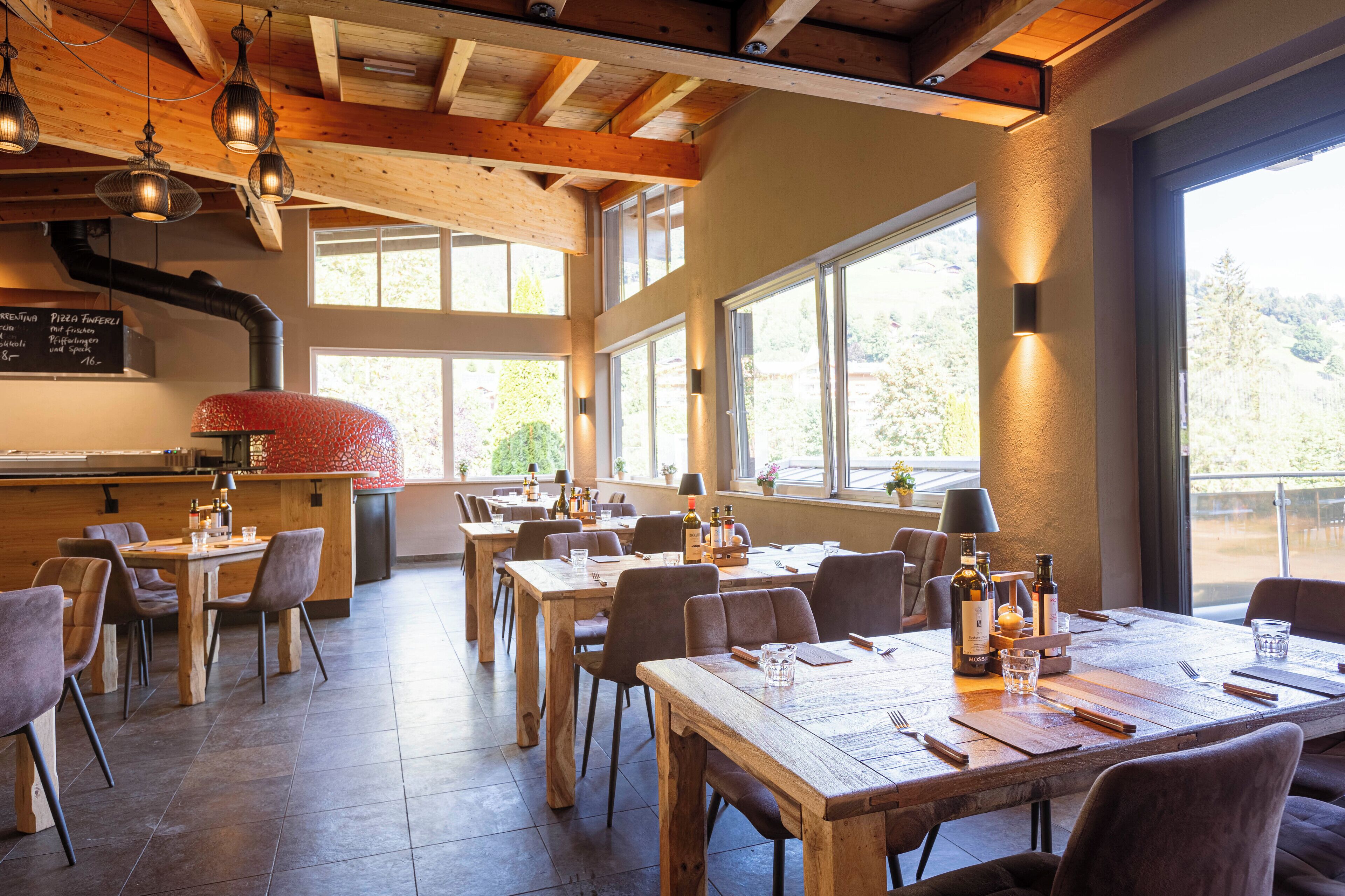 A restaurant with wooden tables and chairs, large windows, and hanging lights.