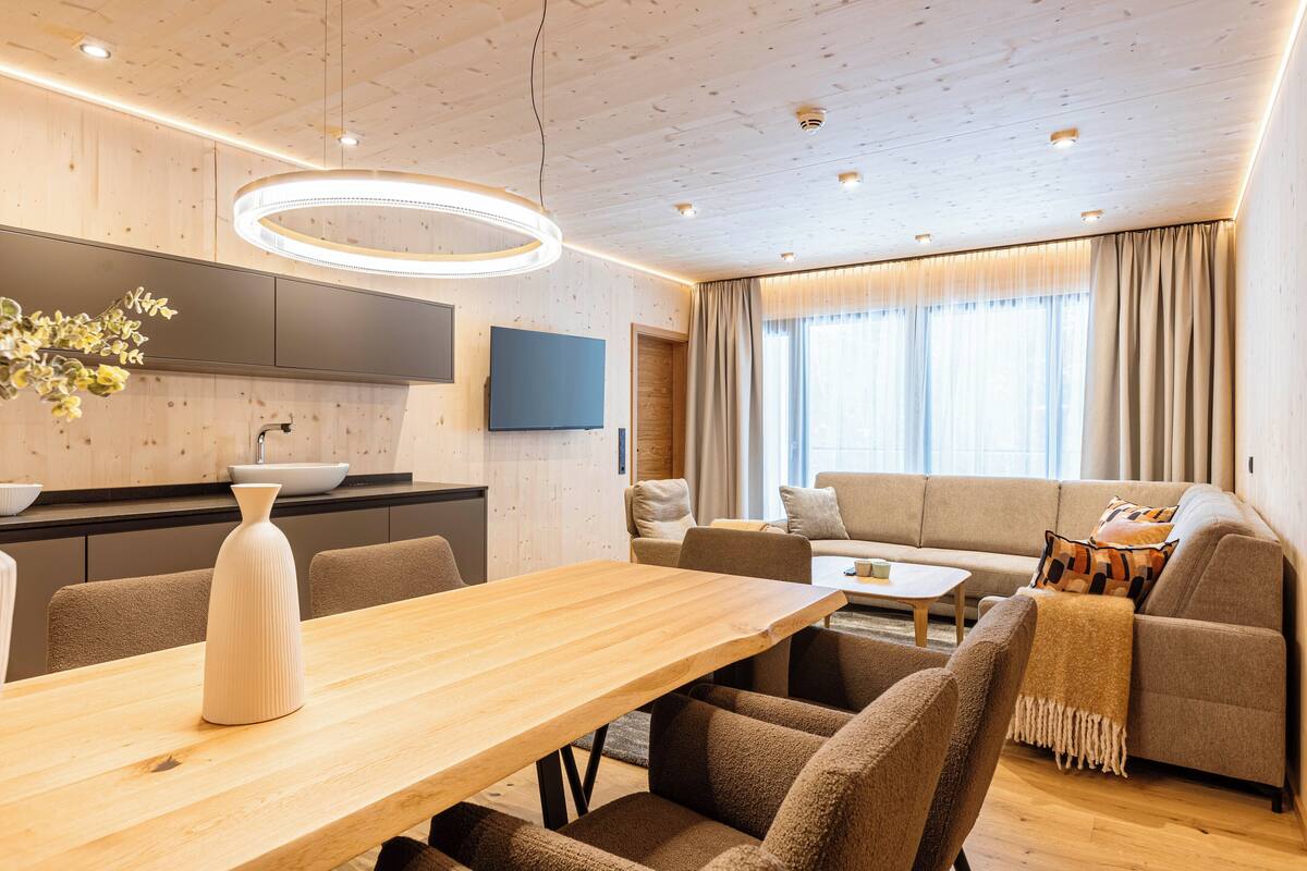 Ein modernes Wohnzimmer mit Esstisch aus Holz, einer Couch und einem Fernseher.