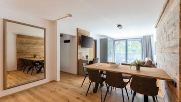 A modern dining area with a wooden table and chairs, a large mirror, and a television on the wall.