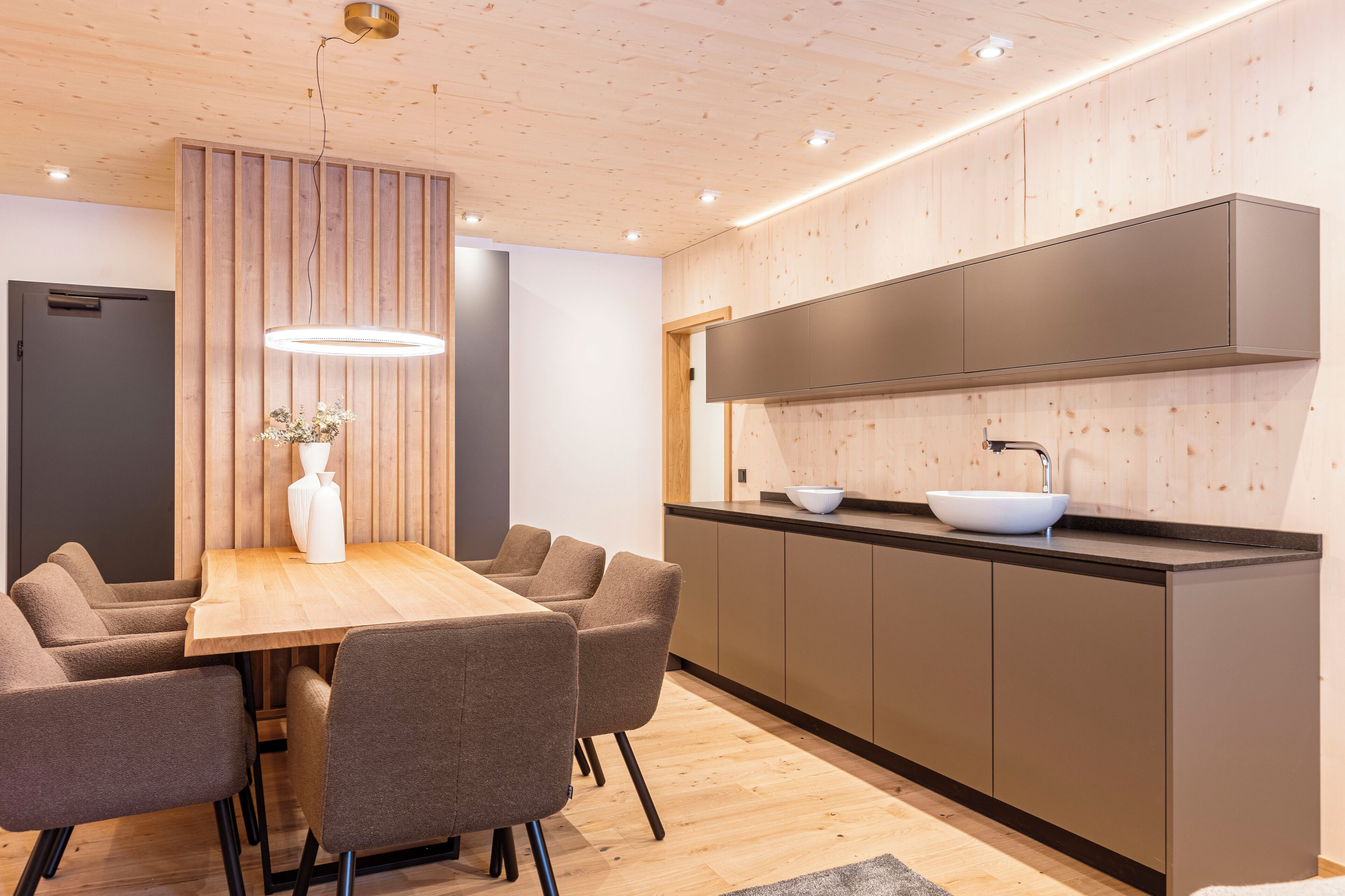 Eine moderne Küche mit einer Wand aus Holzpaneelen, einer zentralen Kochinsel mit weißer Schüssel und einem Einbauofen.
