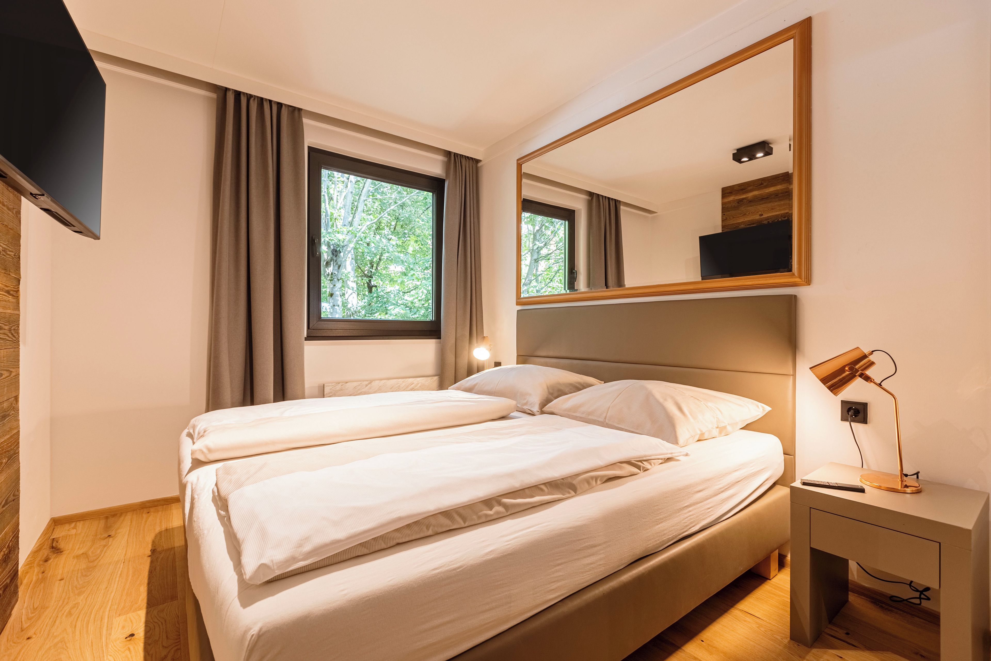 Une chambre à coucher avec un lit, une table de chevet, un miroir et une fenêtre avec des rideaux.