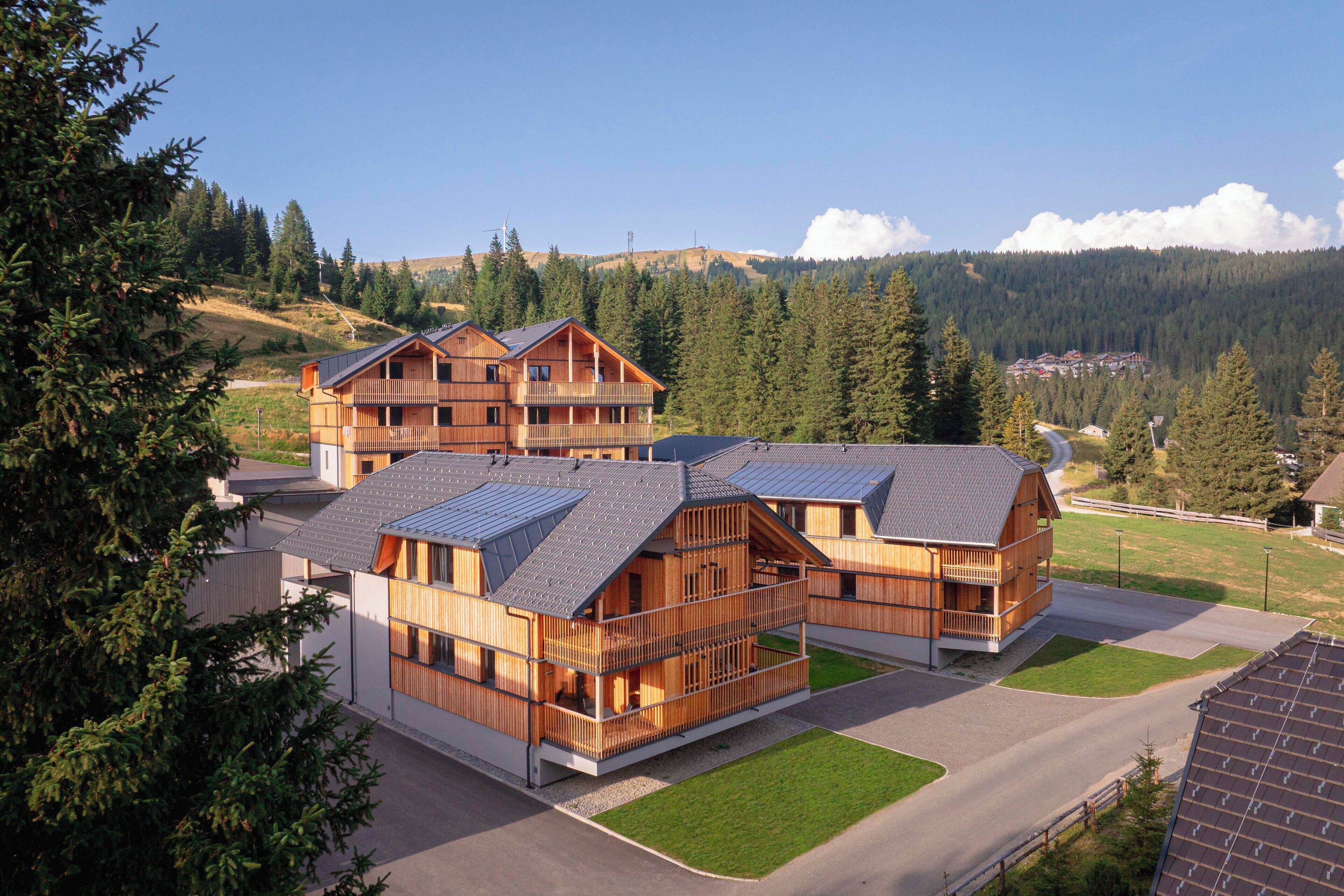 Un chalet en bois à plusieurs étages, doté de balcons, situé dans une région montagneuse sous un ciel dégagé.