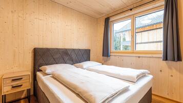 Un dormitorio con cabecera de madera, una mesita de noche pequeña y una ventana con cortinas.