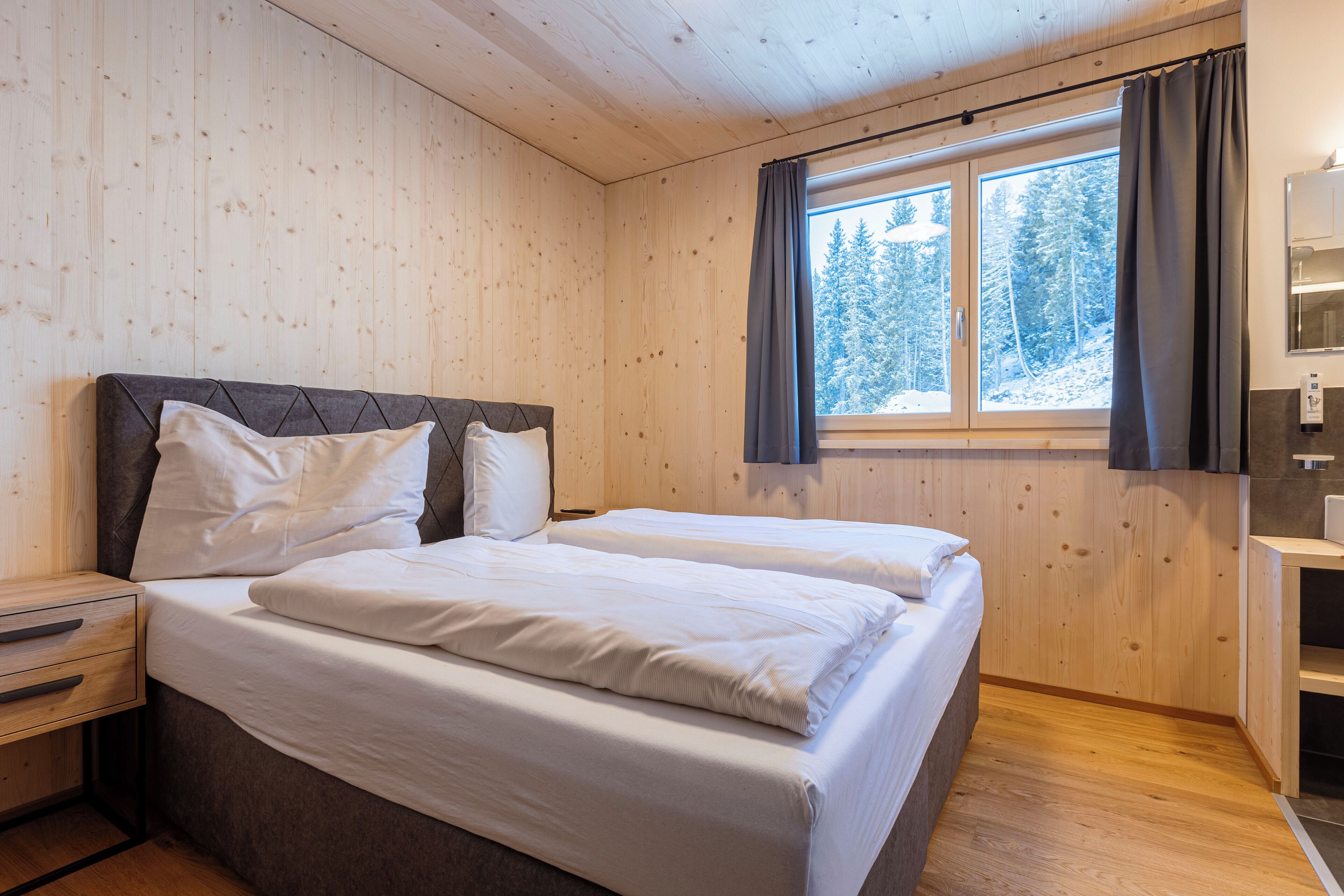 Une chambre dans un chalet en bois, avec deux lits, une table de chevet et une fenêtre avec des rideaux.