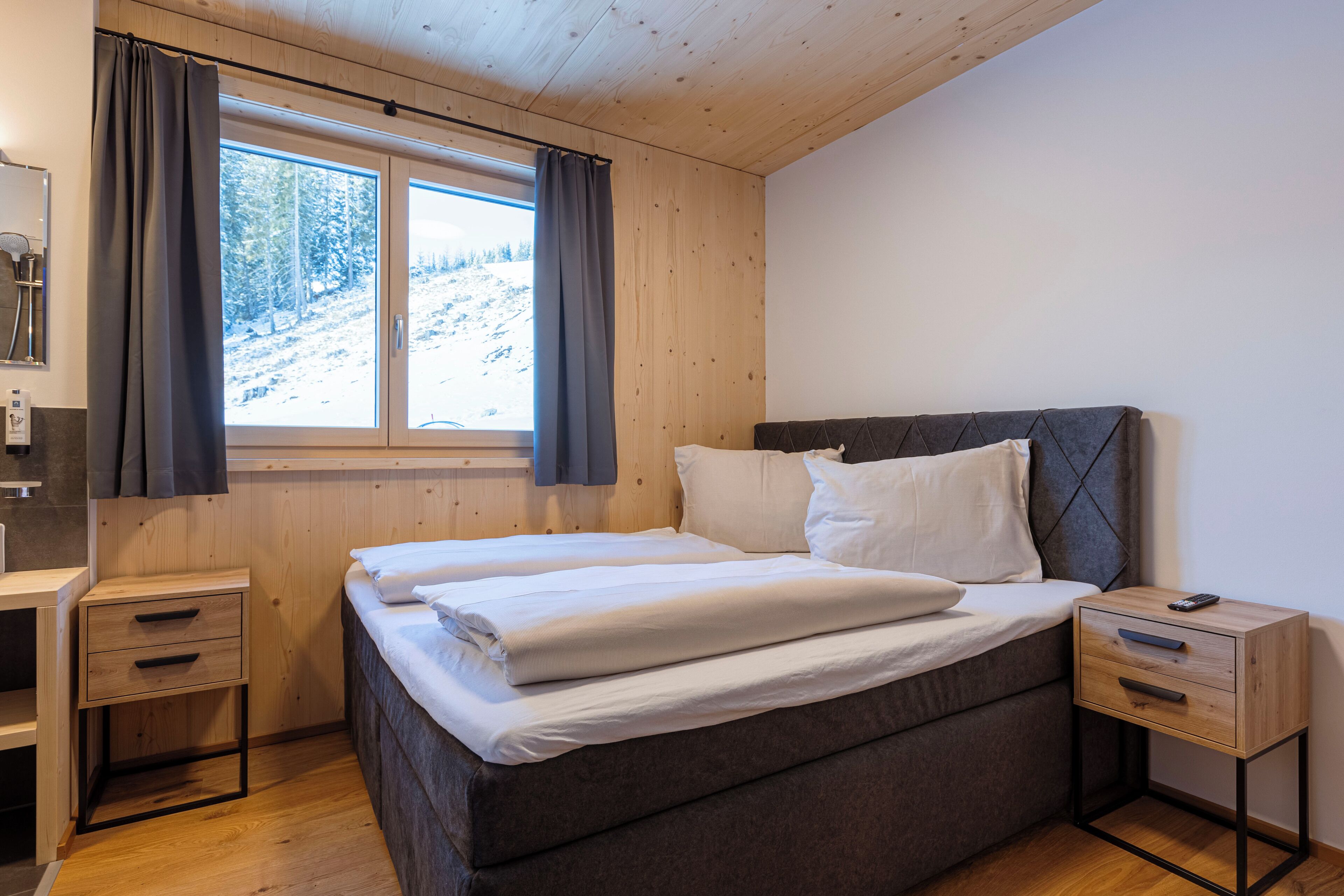 A bedroom with a bed, a bedside table, a window with curtains, and a view of a snowy landscape.
