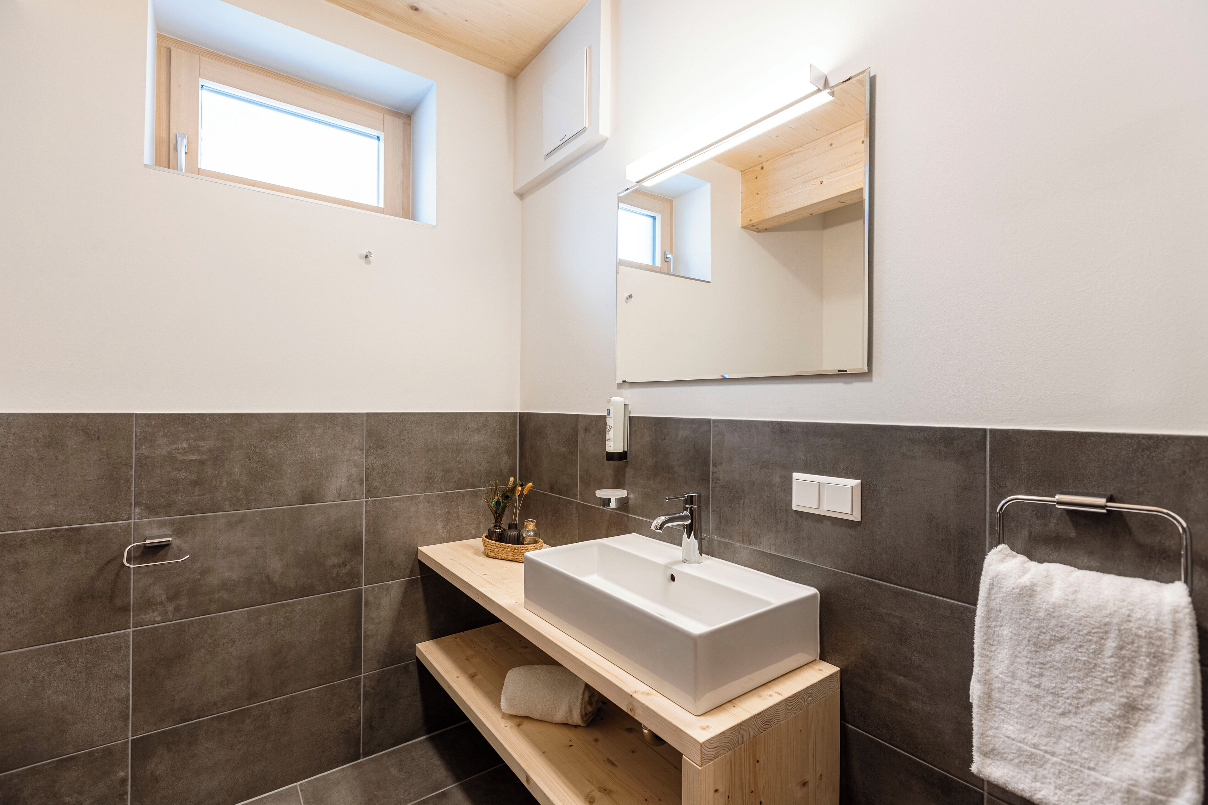 Un baño moderno con un lavamanos grande de color blanco, un mueble de tocador de madera, un perchero y un tragaluz.