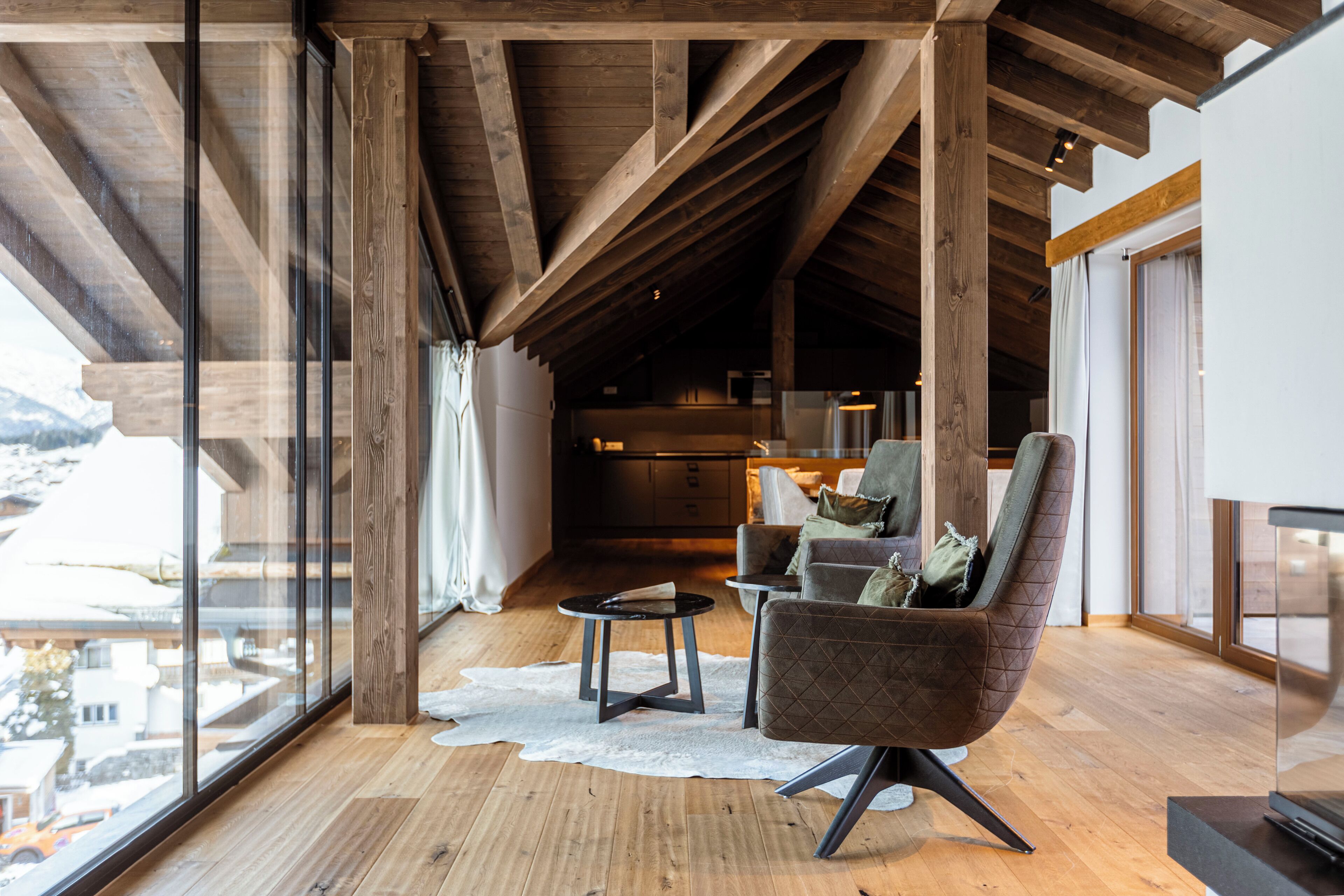 A modern interior with a wooden ceiling, large windows, a cozy seating area, and a view of the outdoors.