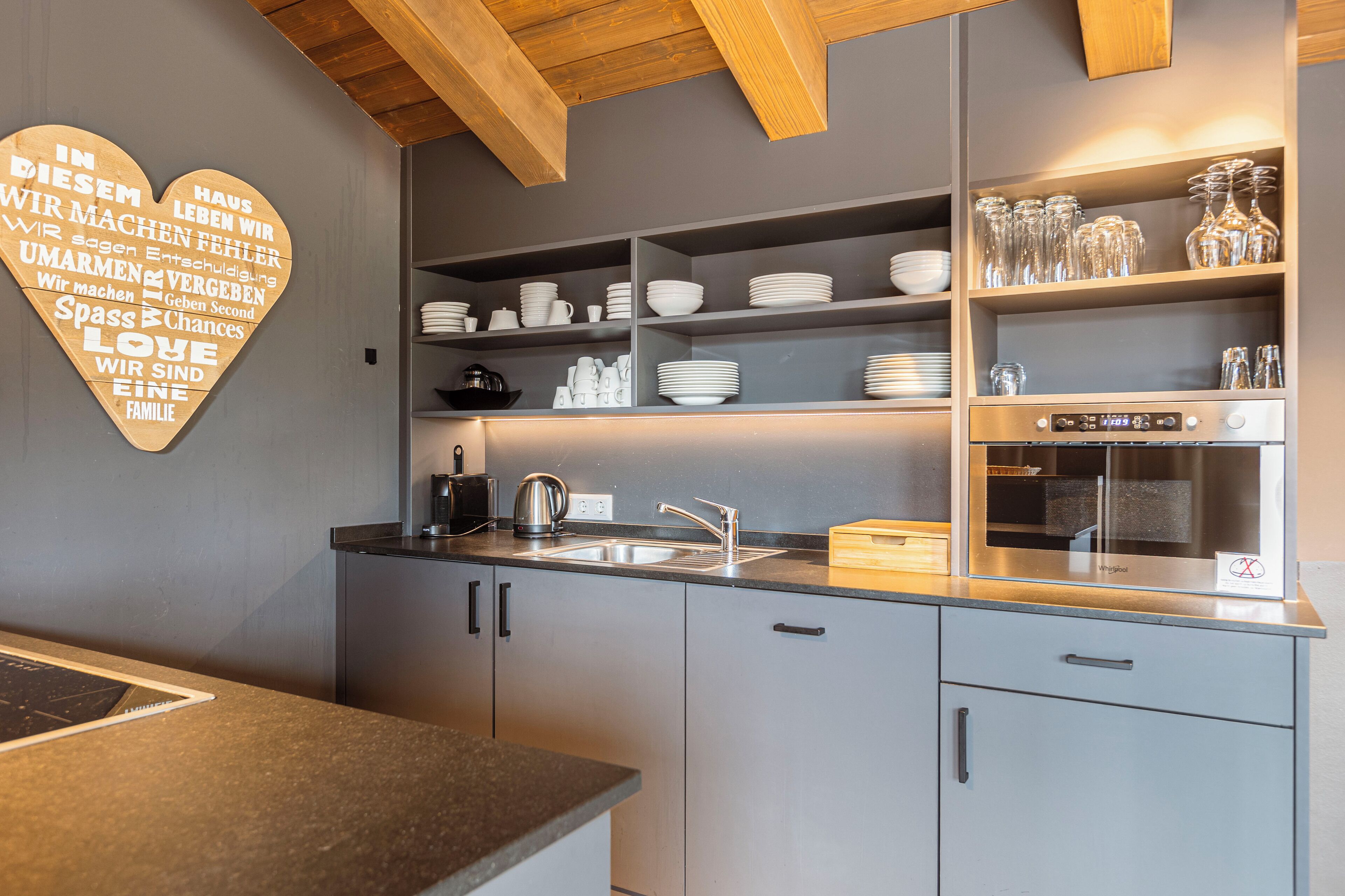 A modern kitchen with grey cabinets, a stainless steel sink, and a heart-shaped wall decoration.