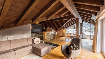 A spacious loft with a high ceiling, wooden beams, a modern kitchen, and a large window offering a view of the outdoors.