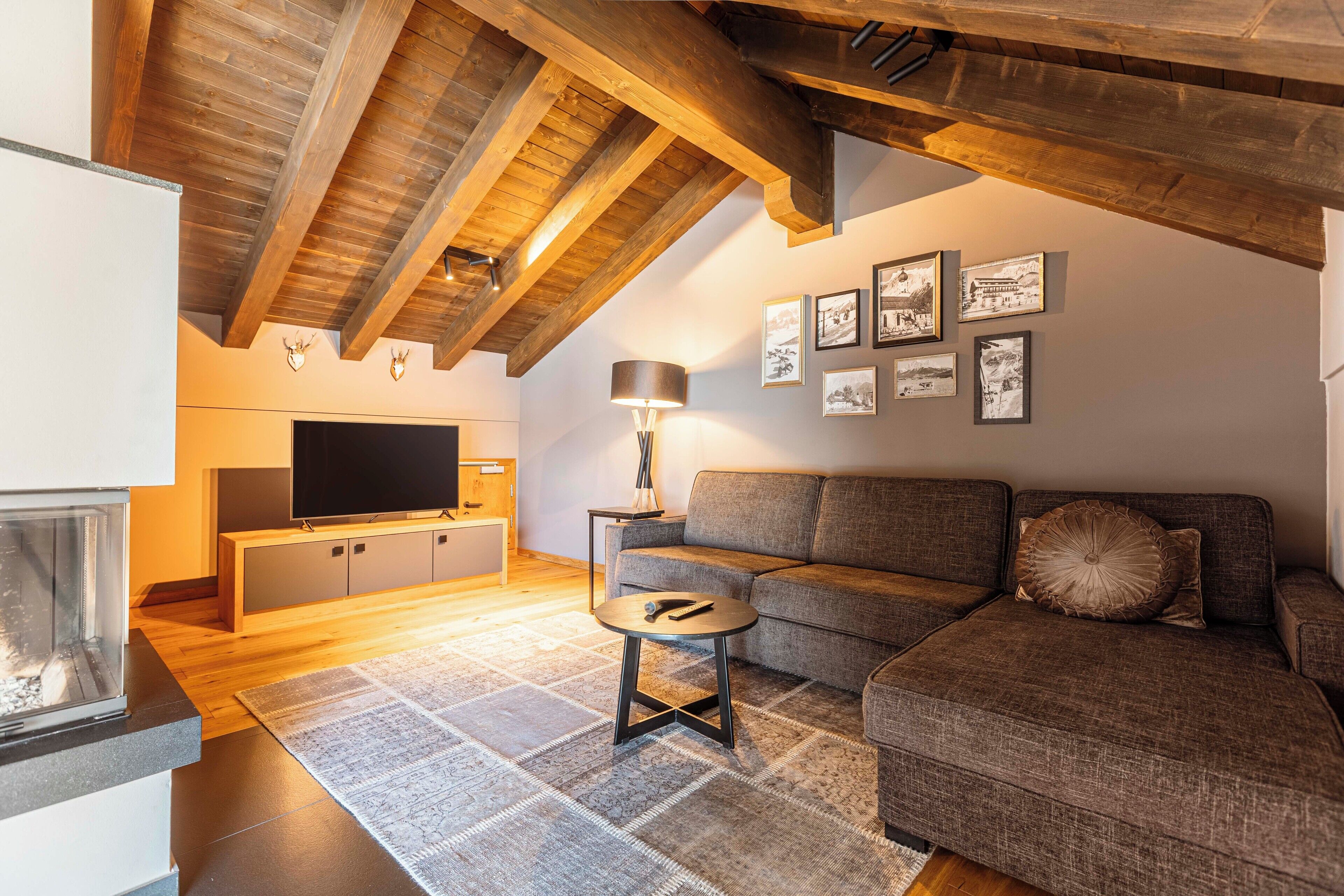 A modern living room with a wooden ceiling, a flat-screen TV, a sofa, a coffee table, and a fireplace.