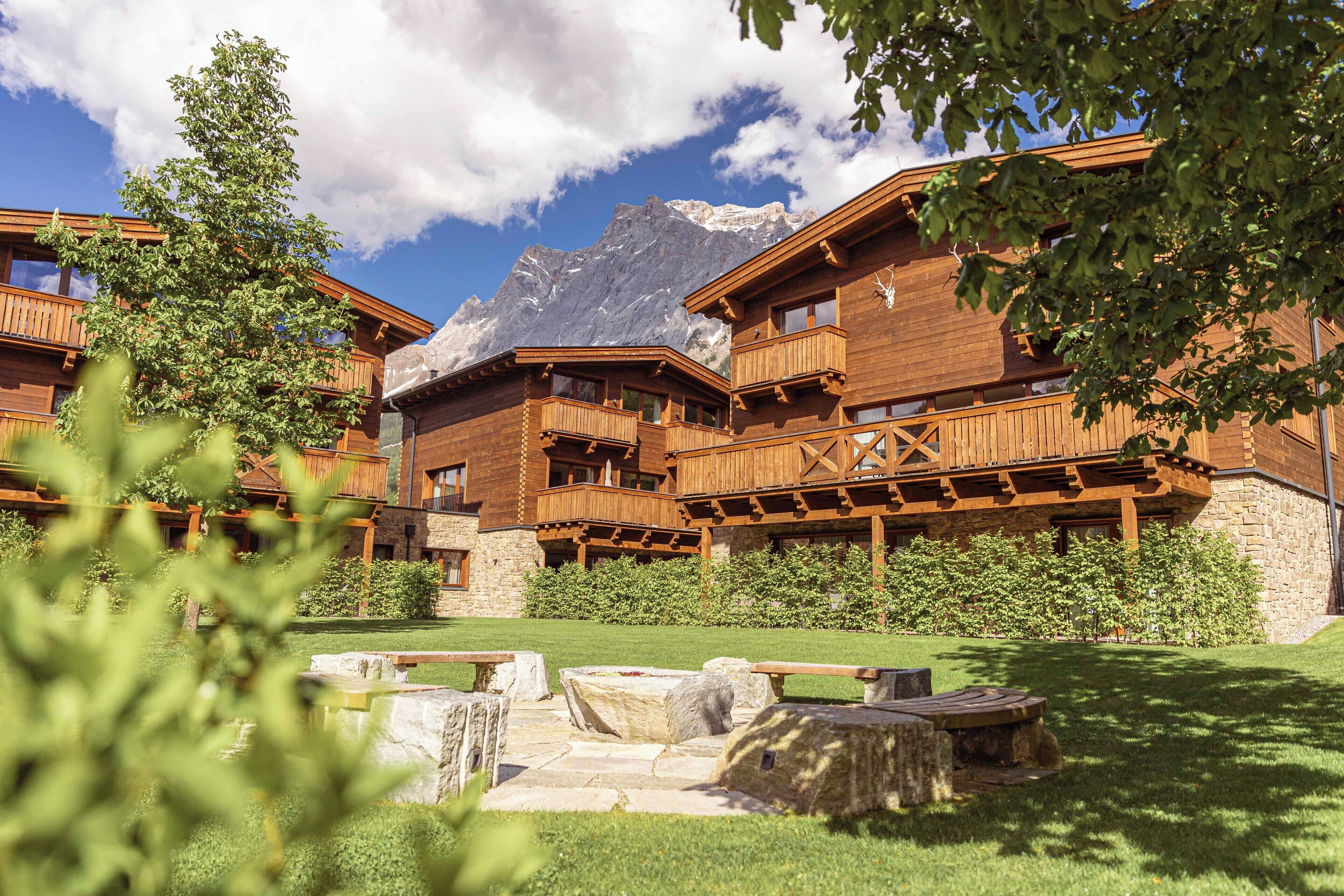 A wooden chalet with balconies, stone walls, and a mountain backdrop.