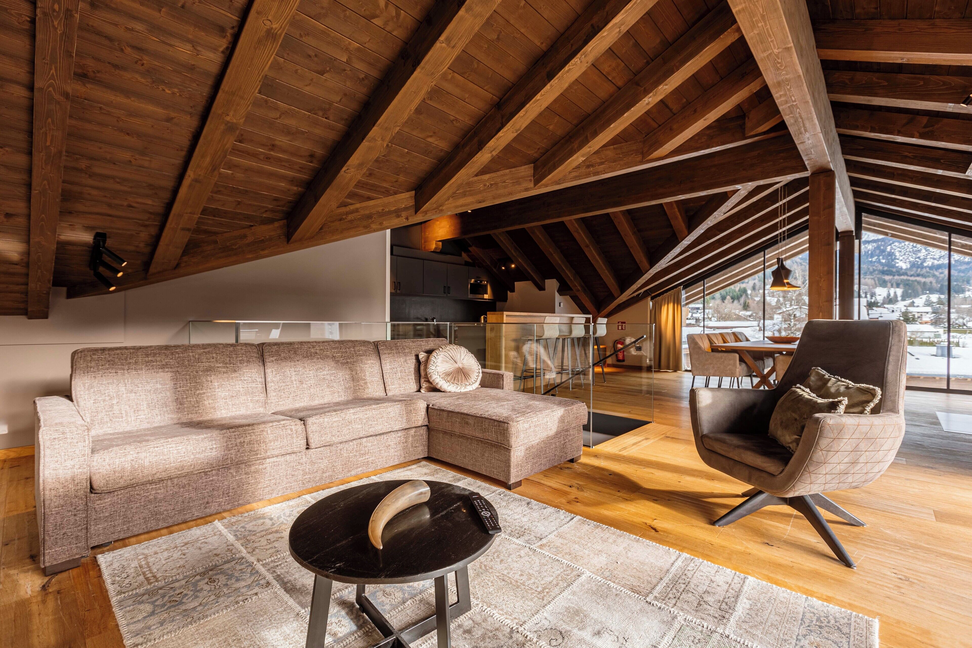 A modern living room with a wooden ceiling, a sectional sofa, a round coffee table, and a comfortable armchair.