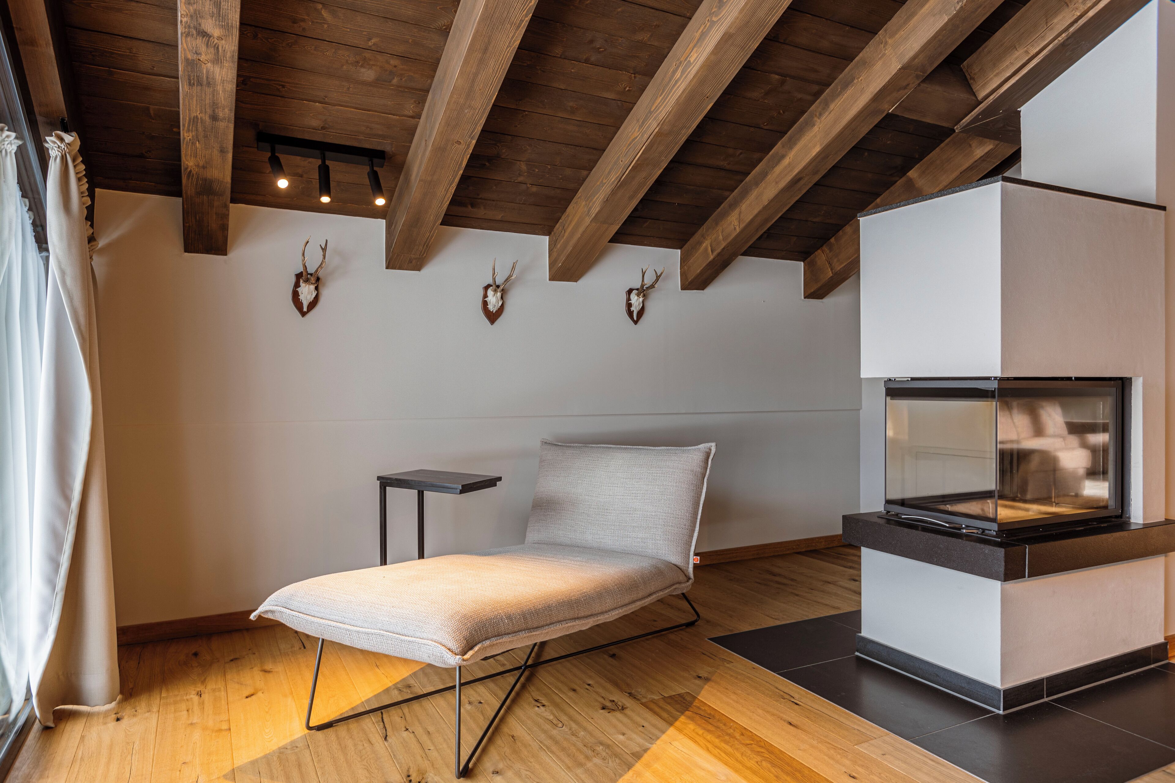 Una habitación moderna con sofá, chimenea, vigas de madera y cornamentas de ciervo en la pared.