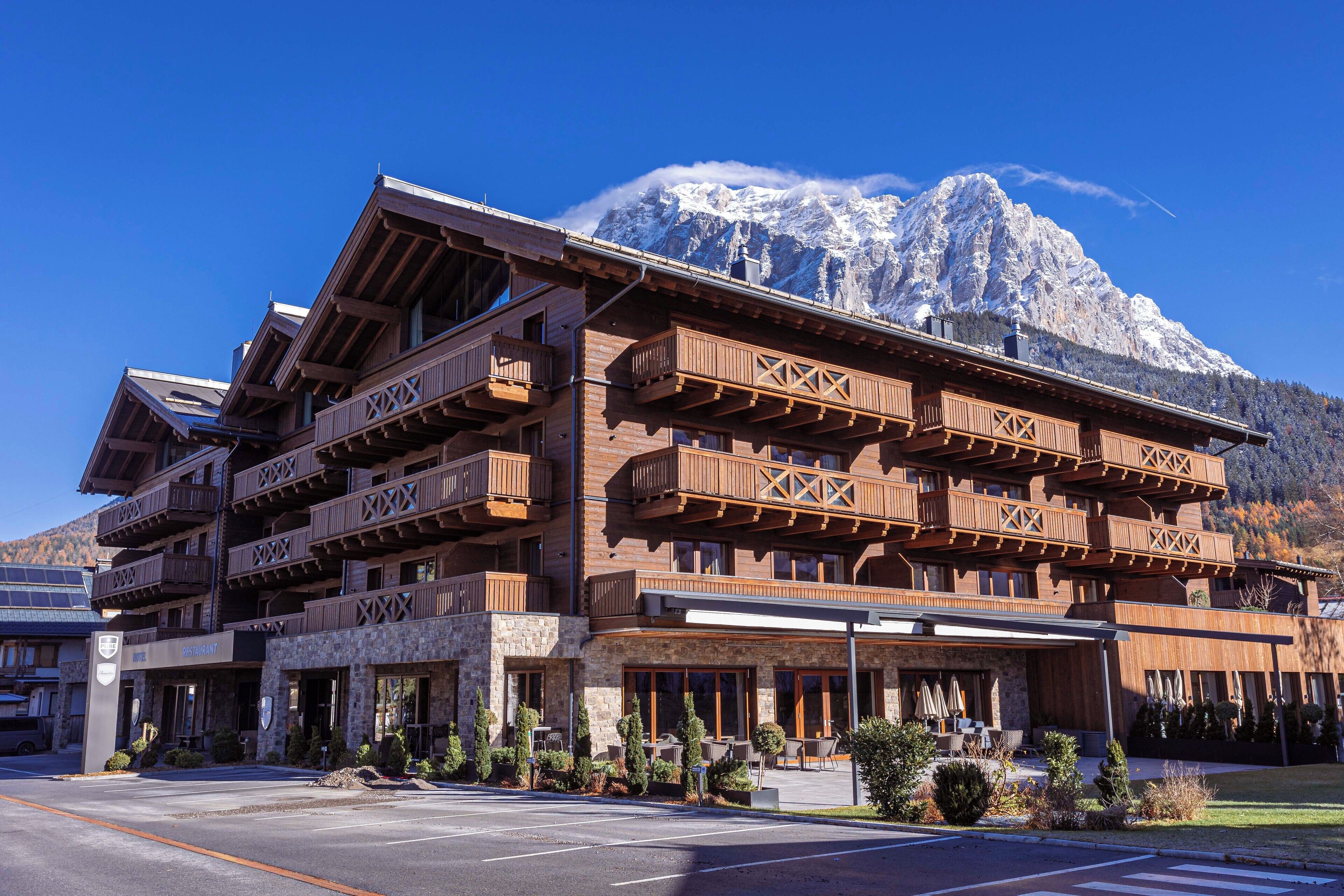 A multi-story wooden building with balconies, a restaurant sign, and a mountain backdrop.