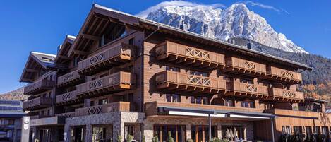 A multi-story wooden building with balconies, a restaurant sign, and a mountain backdrop.