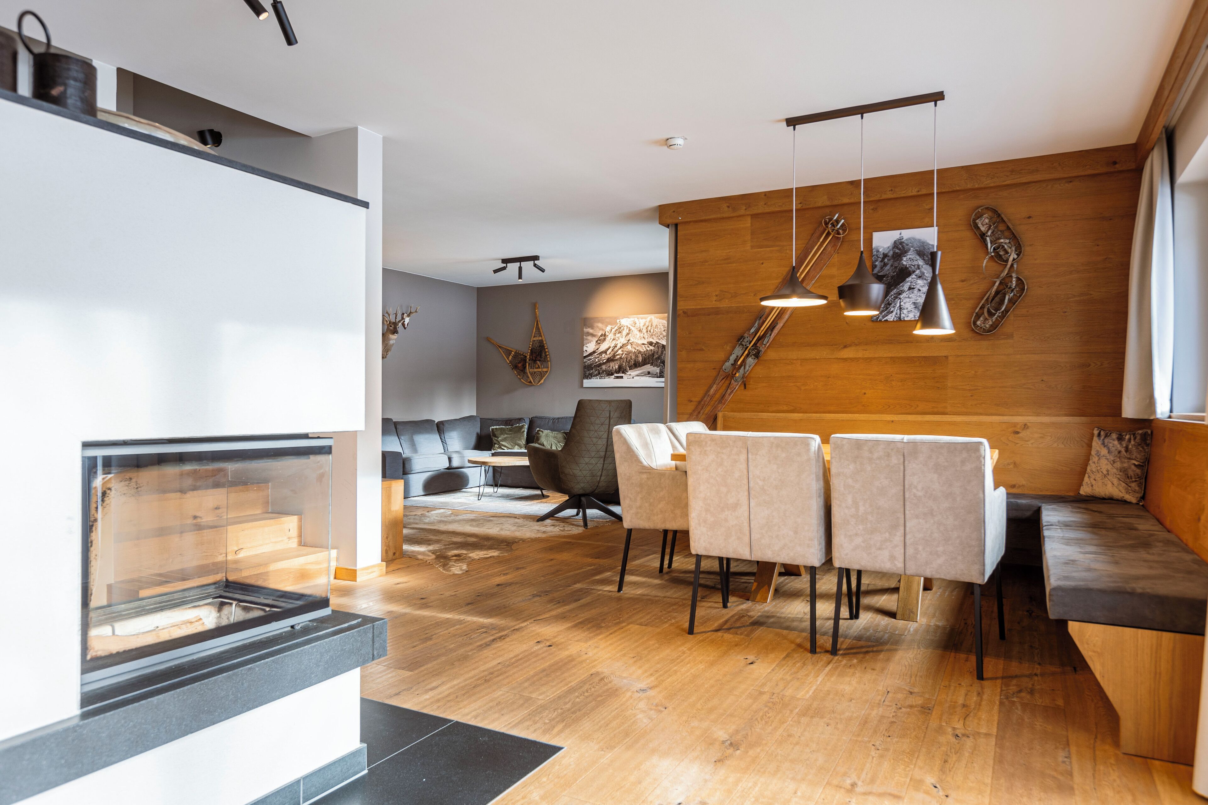 A modern living room with a wooden wall, a dining area with chairs and a bench, and a fireplace.
