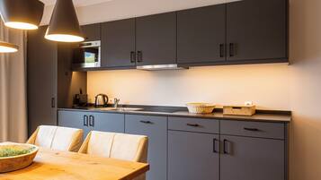 A modern kitchen with grey cabinets, a wooden dining table, and pendant lighting.