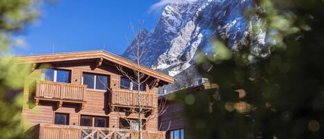 Un chalet en bois doté de plusieurs balcons, situé au pied de montagnes enneigées.