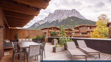A wooden deck with a table and chairs, a wooden building with balconies, and a mountain in the background.