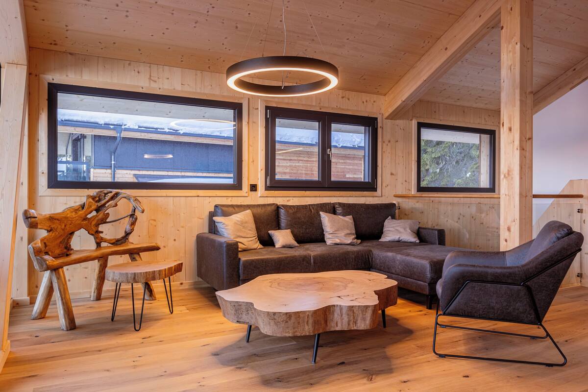 A cozy cabin interior with a wooden floor, a sectional sofa, a leather armchair, and a unique wooden coffee table.