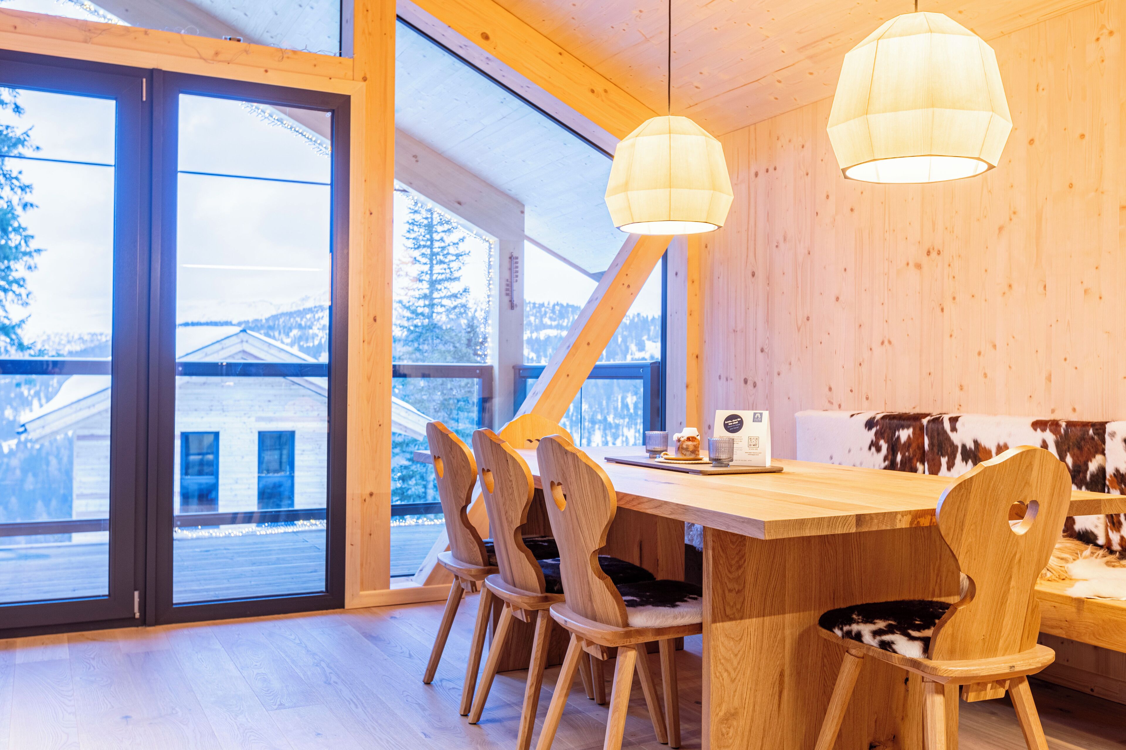 Un coin repas en bois avec une grande table, des chaises et un banc en peau de vache.