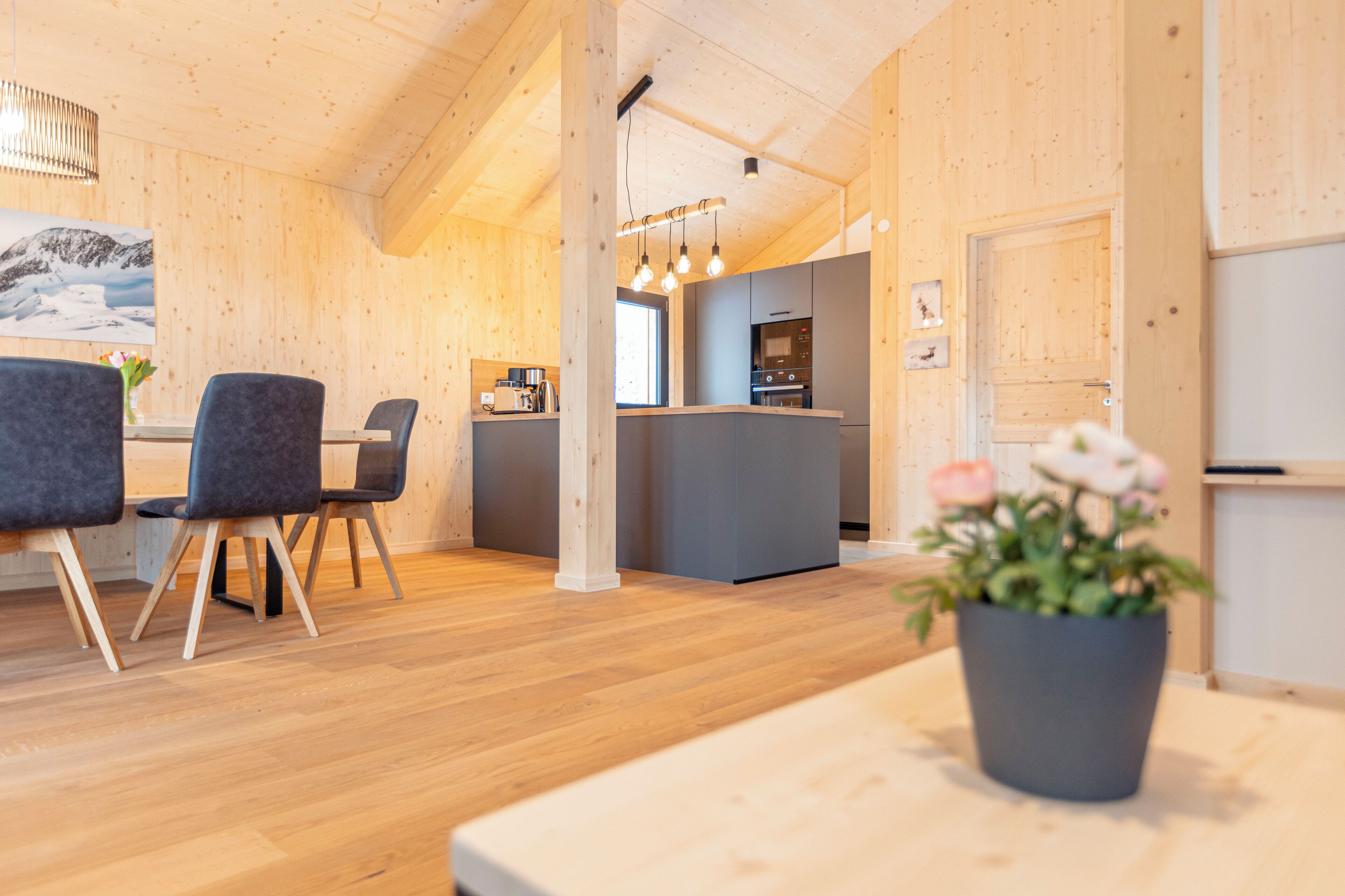 A modern interior with wooden walls, a dining area with chairs, a kitchen with a counter, and a potted plant.