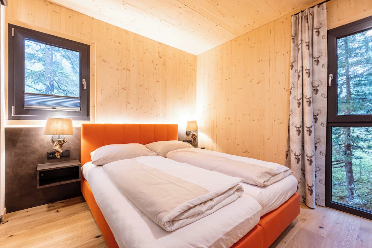 A wooden cabin bedroom with a bed, nightstands, and a window with curtains.