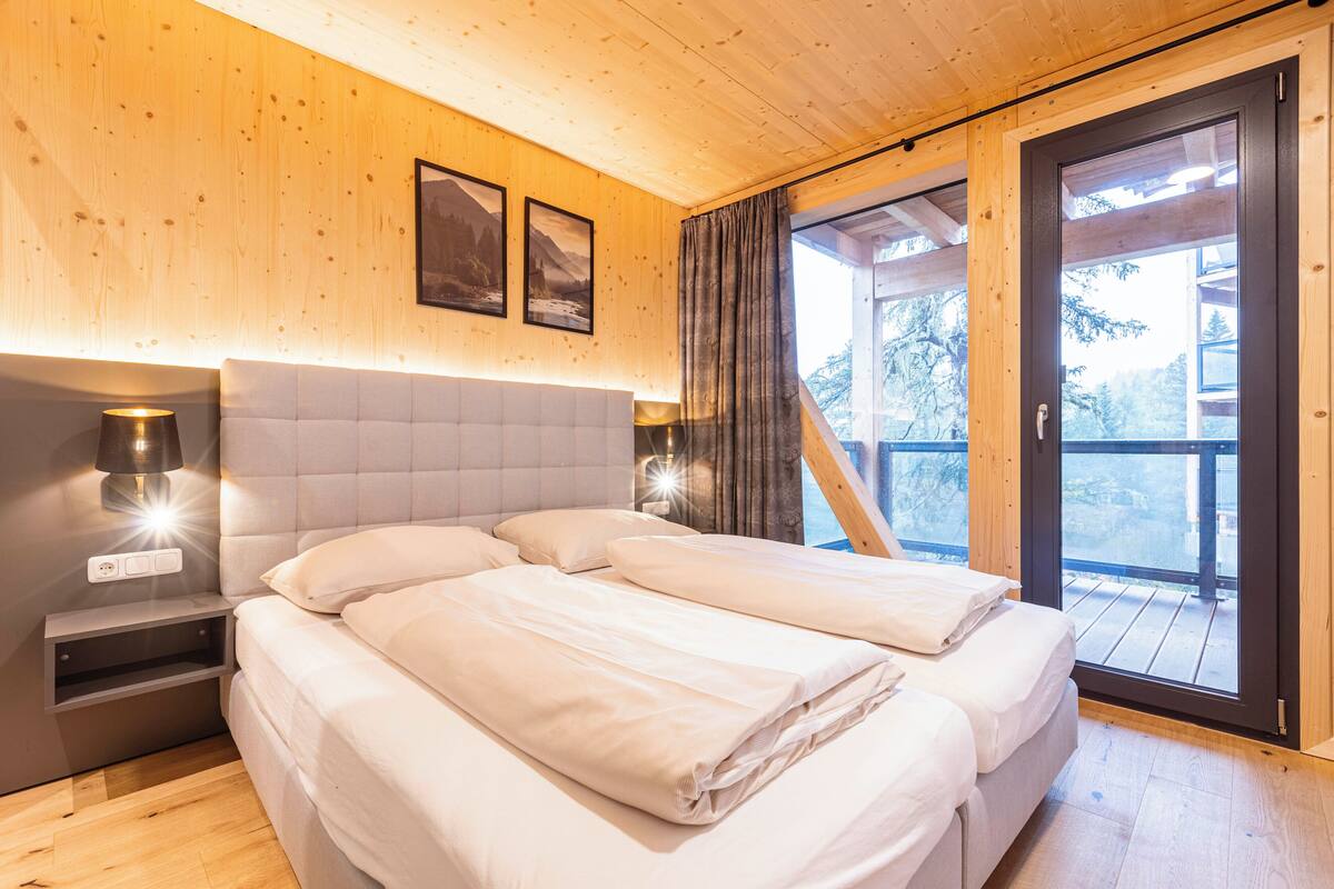 A bedroom with two beds, wooden walls, a nightstand, and a window with curtains.