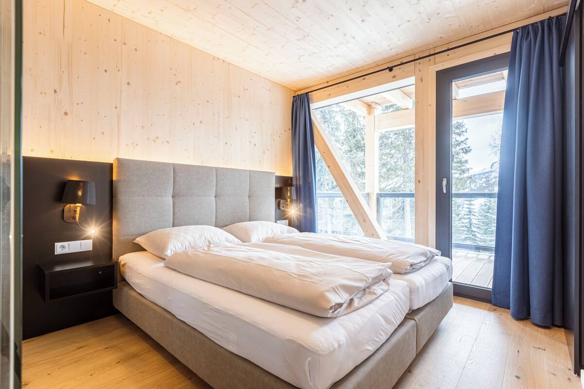 A modern bedroom with a large bed, wooden walls, and a view of the outdoors.