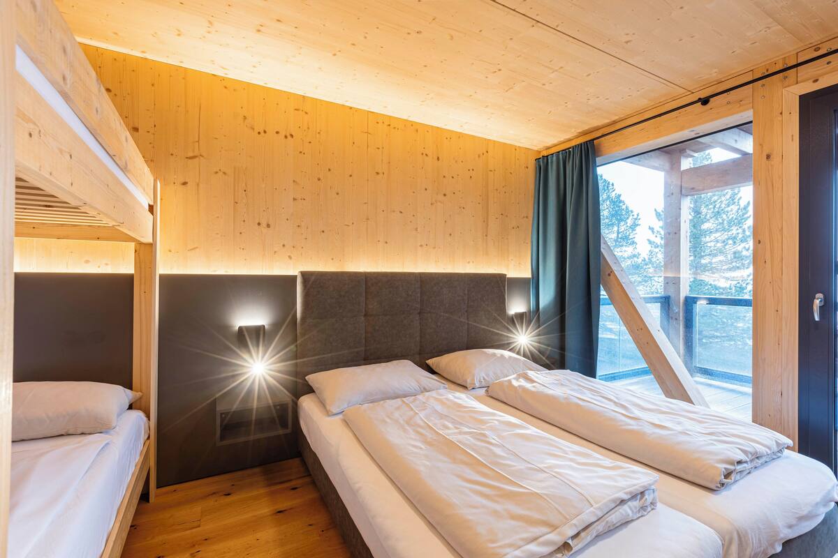 A wooden cabin room with two beds, a built-in bench, and a large window with curtains.