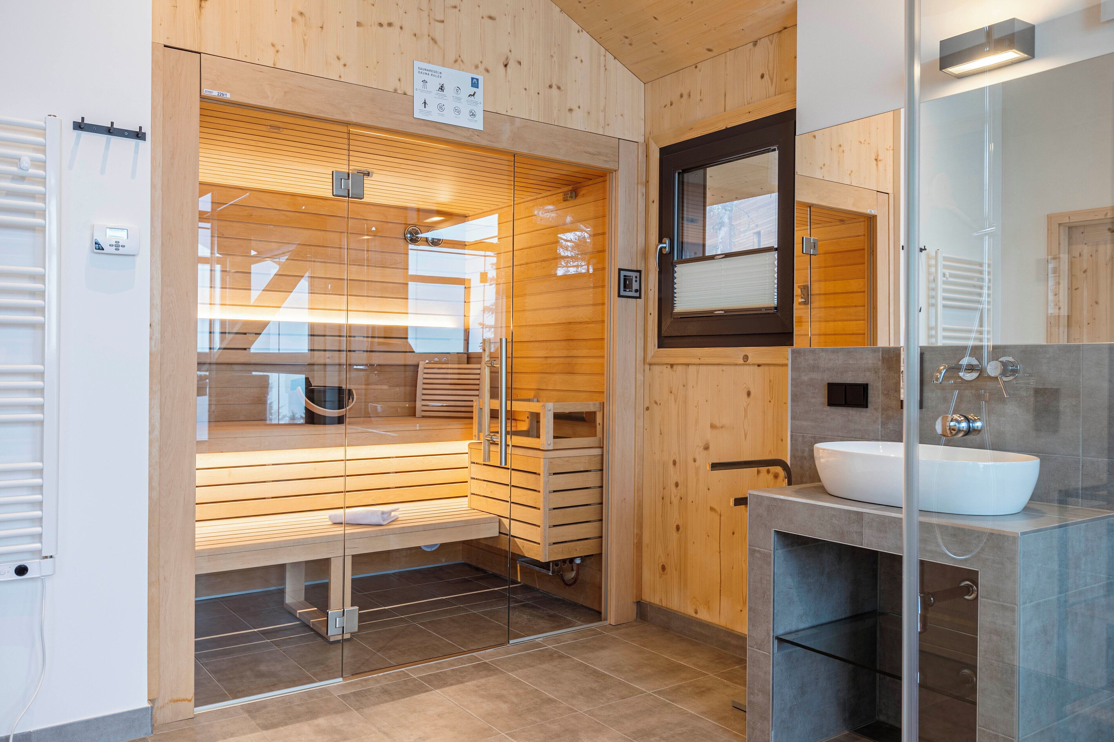 A modern bathroom with a glass-enclosed sauna, a large mirror, and a sink with a marble countertop.