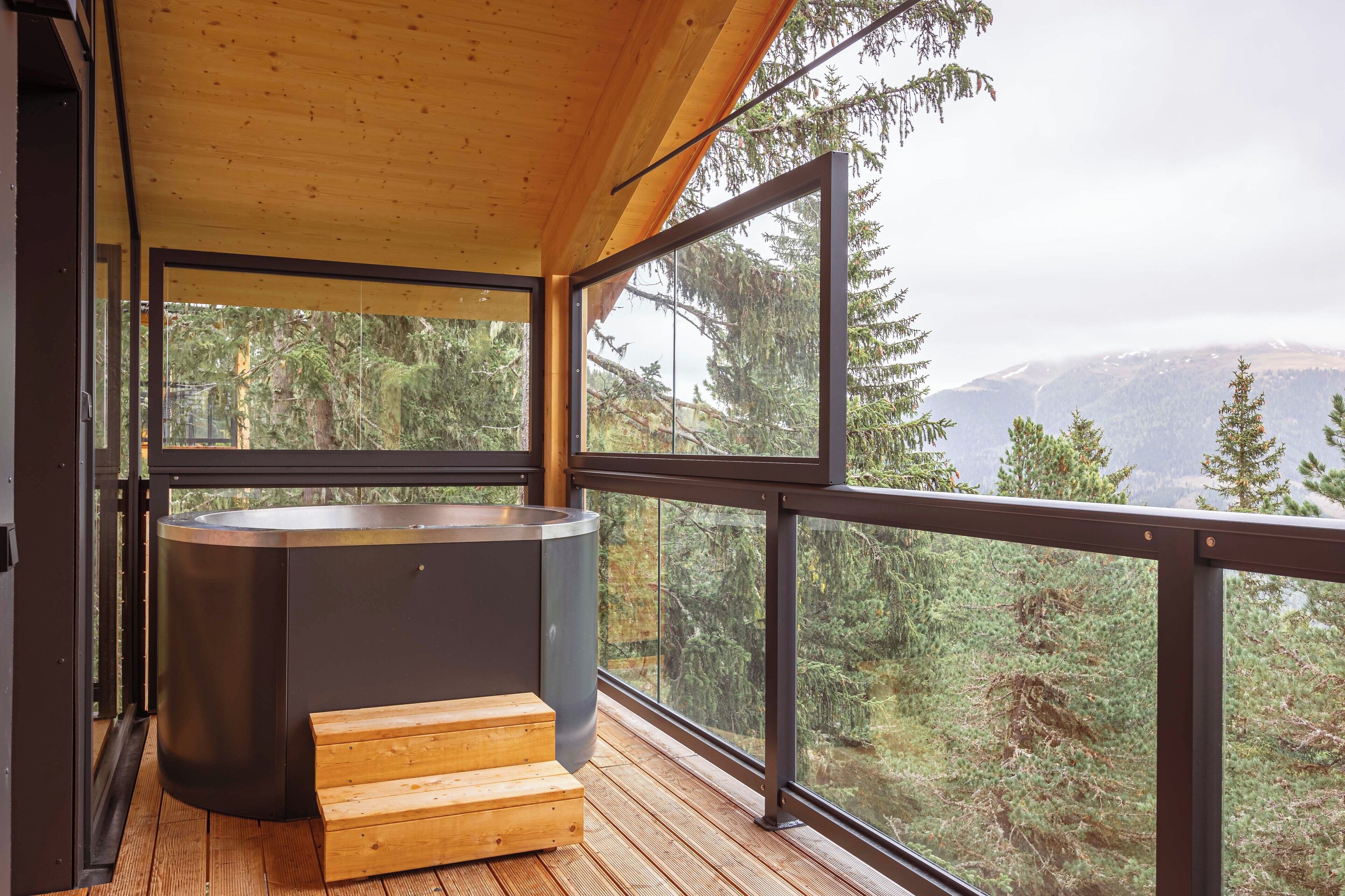 Eine moderne Holzterrasse mit Whirlpool und Holzstufen, mit Blick auf eine bewaldete Berglandschaft.