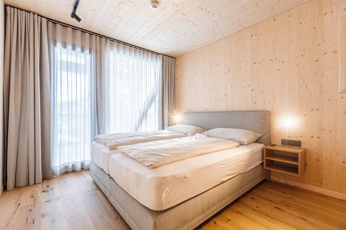 A bedroom with a large bed, wooden walls, and a nightstand with a lamp.