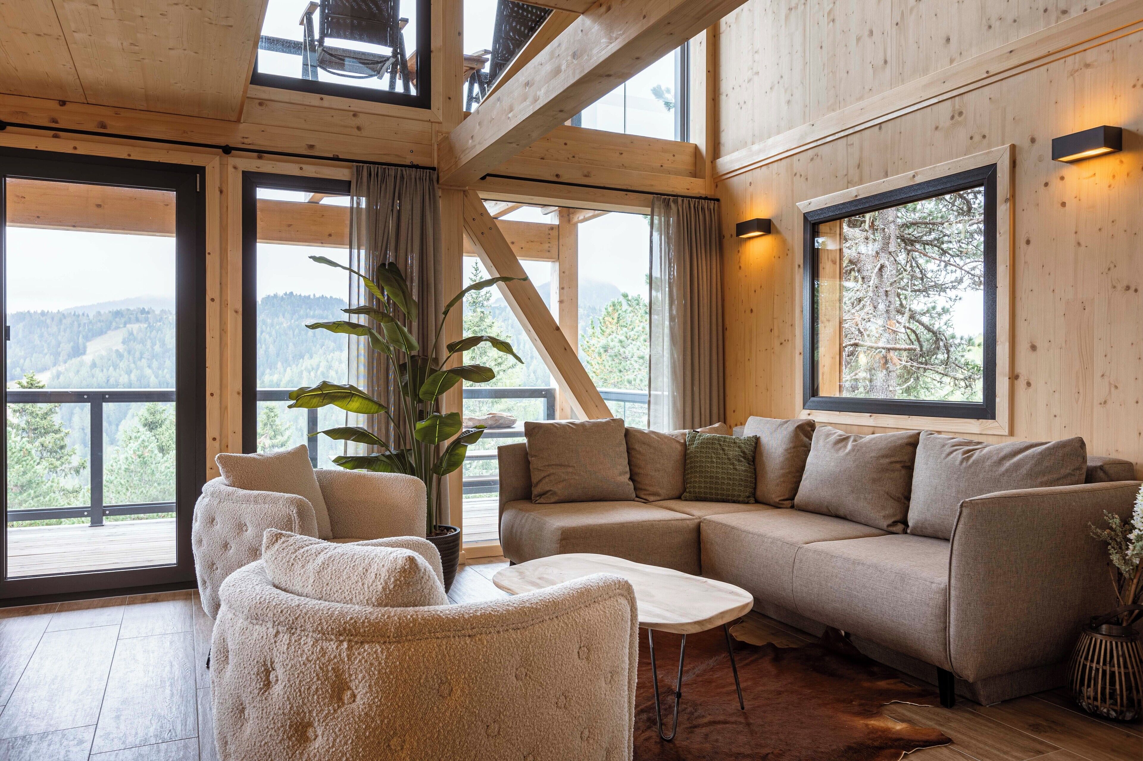 A cozy living room with a sofa, armchairs, and a coffee table. Large windows offer a view of the outdoors.