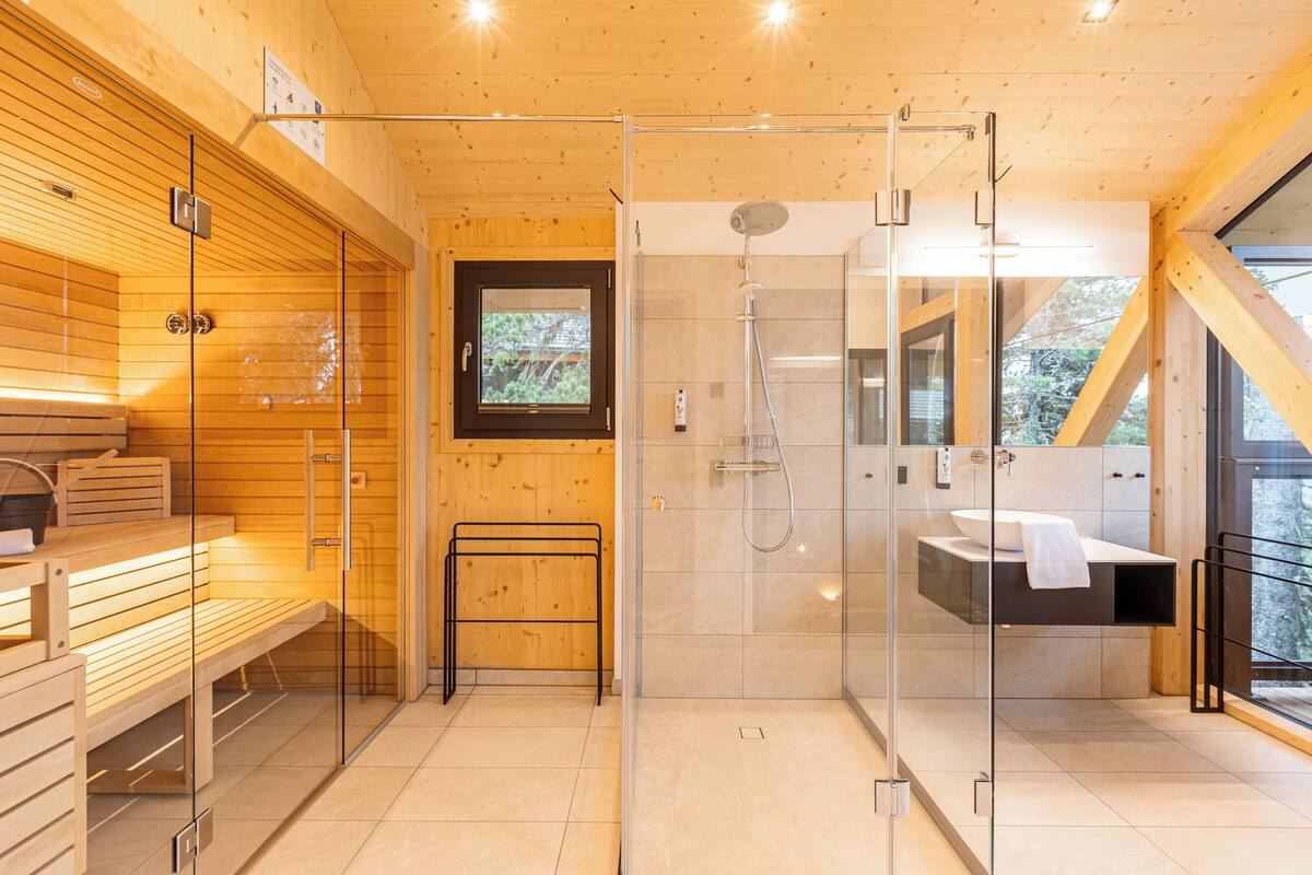 A modern bathroom with a glass-enclosed shower, wooden benches, a bench with a towel, and a view through the glass.