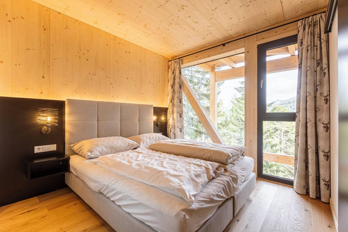 A bedroom with a large bed, wooden walls, a nightstand, and a window with curtains.