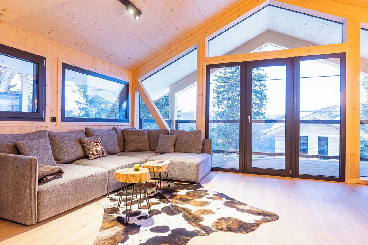 A modern living room with a sectional sofa, a cowhide rug, and large windows offering a view of the outdoors.