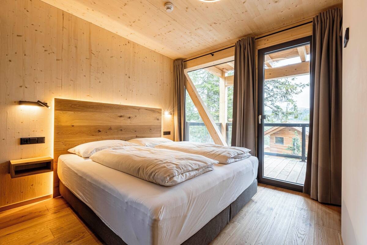 A bedroom with a wooden headboard, a large bed, and a view of a wooden deck outside.