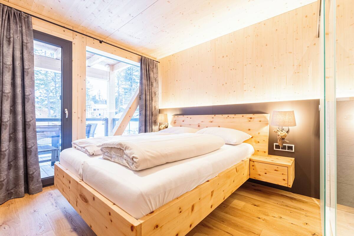 A wooden bed in a room with a glass door leading to an outdoor area.