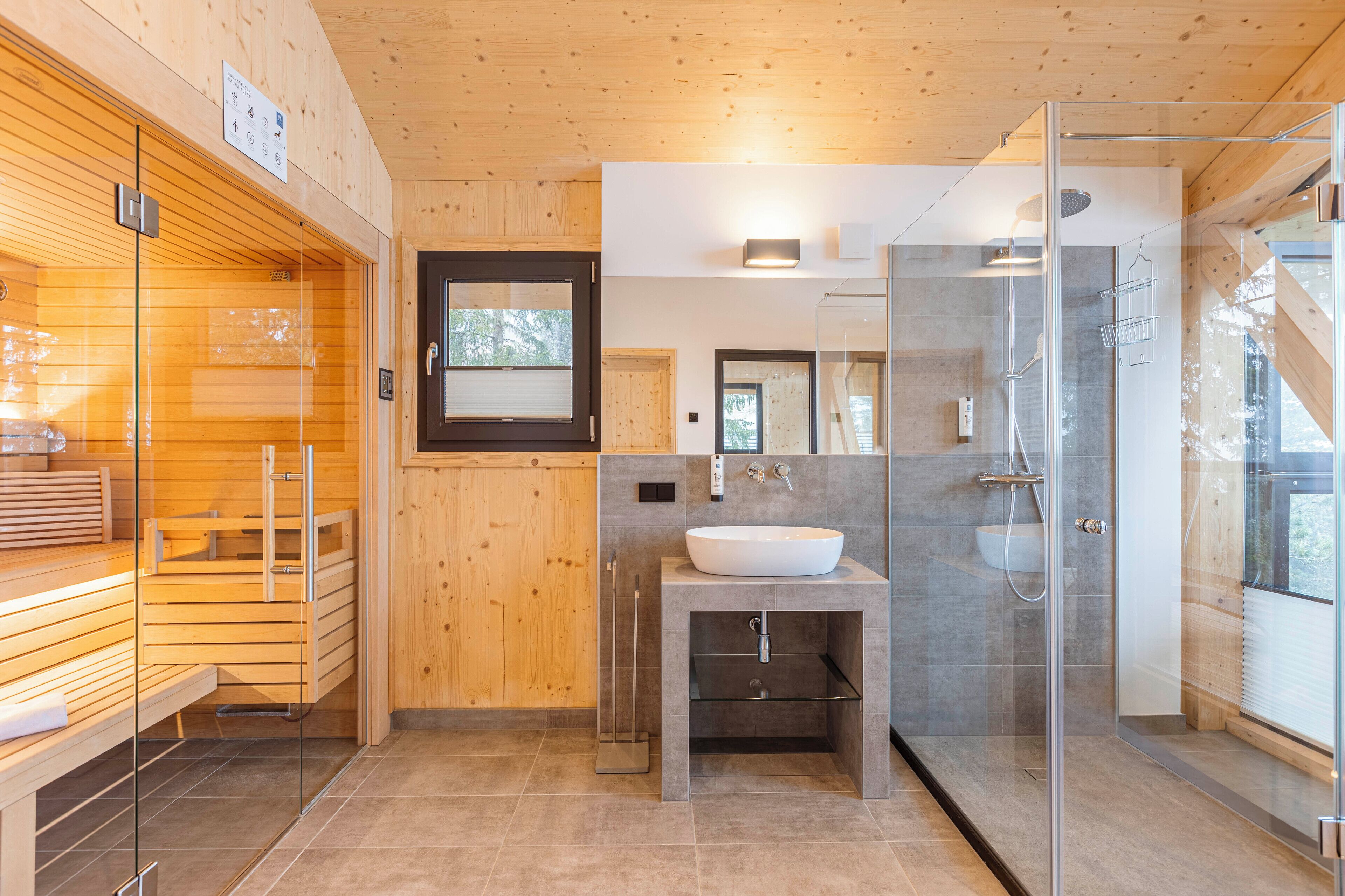A modern bathroom with a wooden sauna, a glass-enclosed shower, and a sink with a mirror above it.