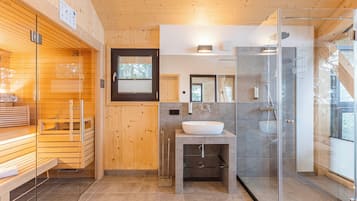 A modern bathroom with a wooden sauna, a glass-enclosed shower, and a sink with a mirror above it.
