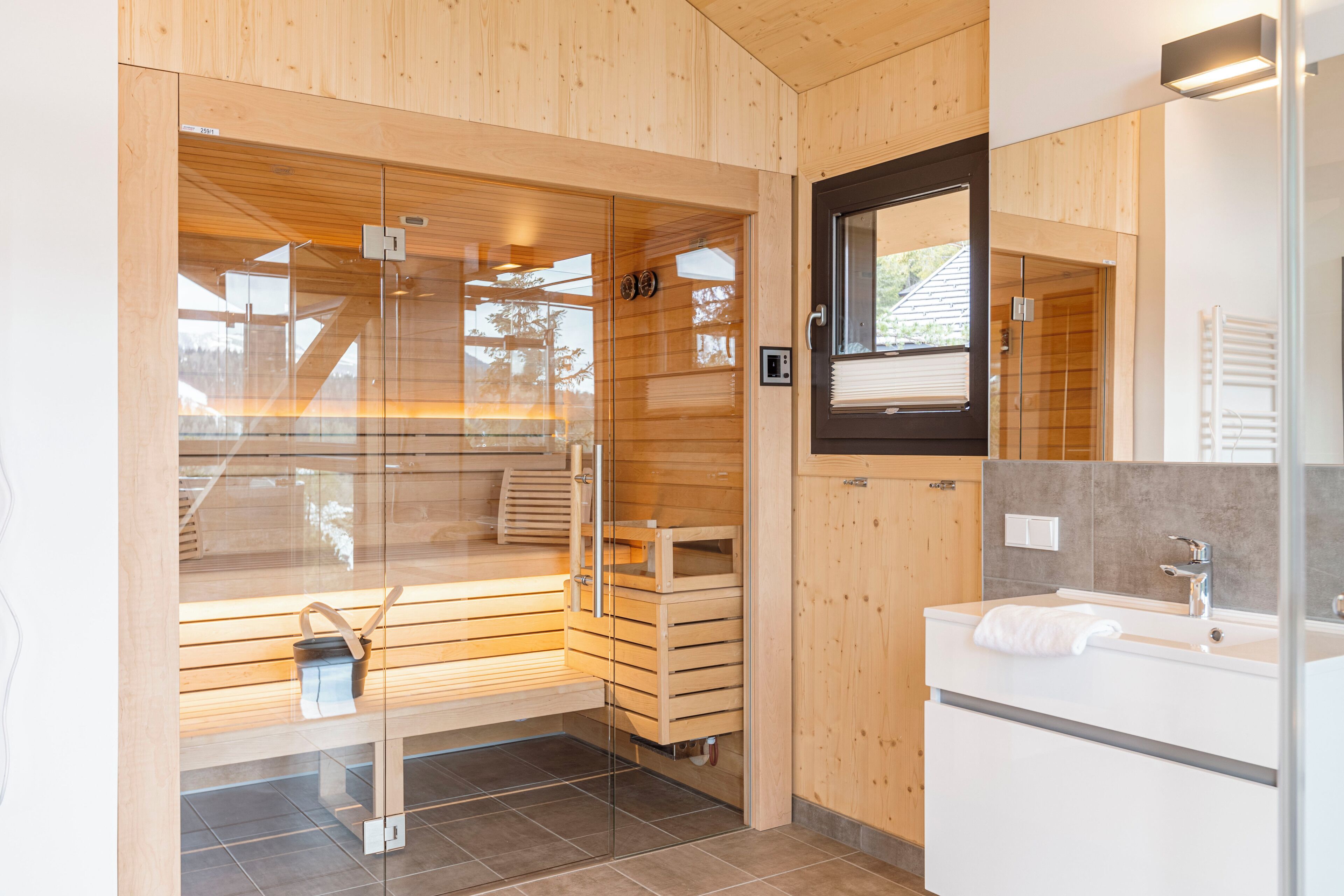 Een moderne badkamer met houten lambrisering, een sauna met glazen wanden, een witte wastafel en een grote spiegel.