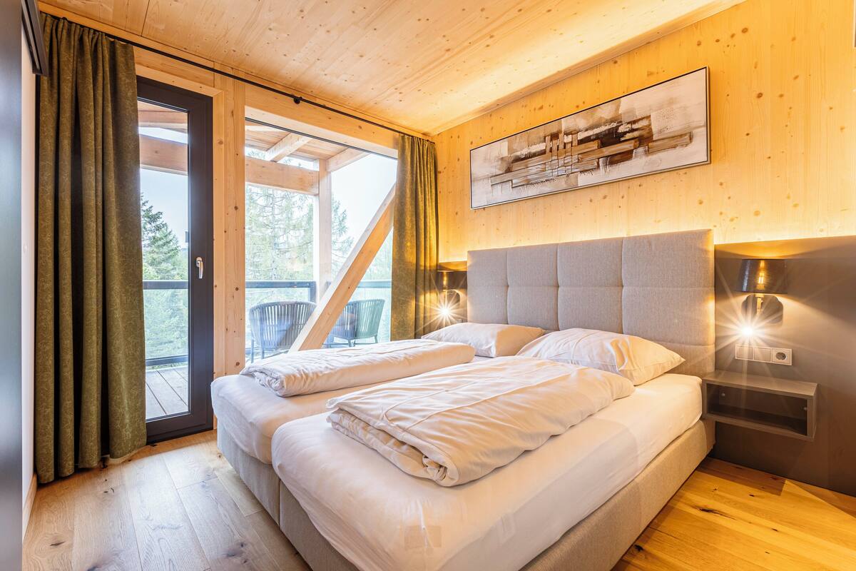 A bedroom with two beds, wooden flooring, a balcony with a chair, and a painting on the wall.