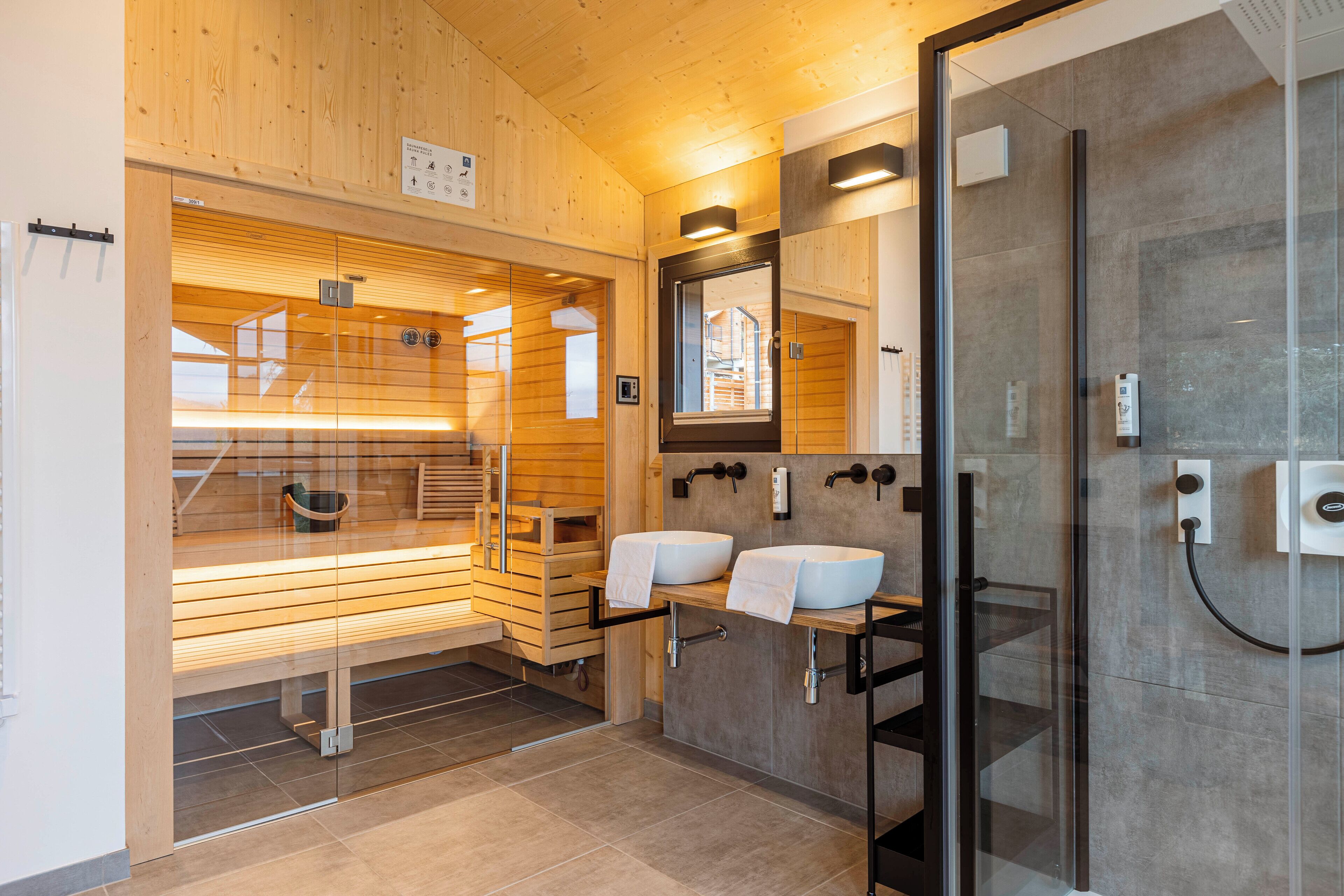 A modern bathroom with wooden walls, a glass shower enclosure, and two sinks.