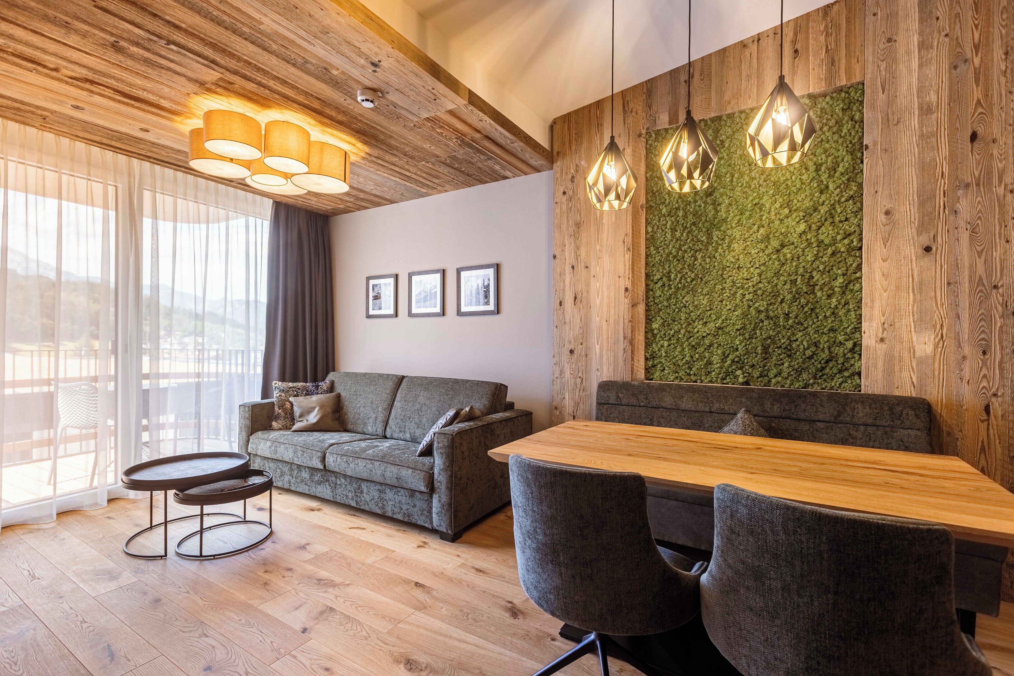 Una sala de estar moderna con techo de madera, pared verde, sofá, mesa de comedor y una pequeña mesa redonda.