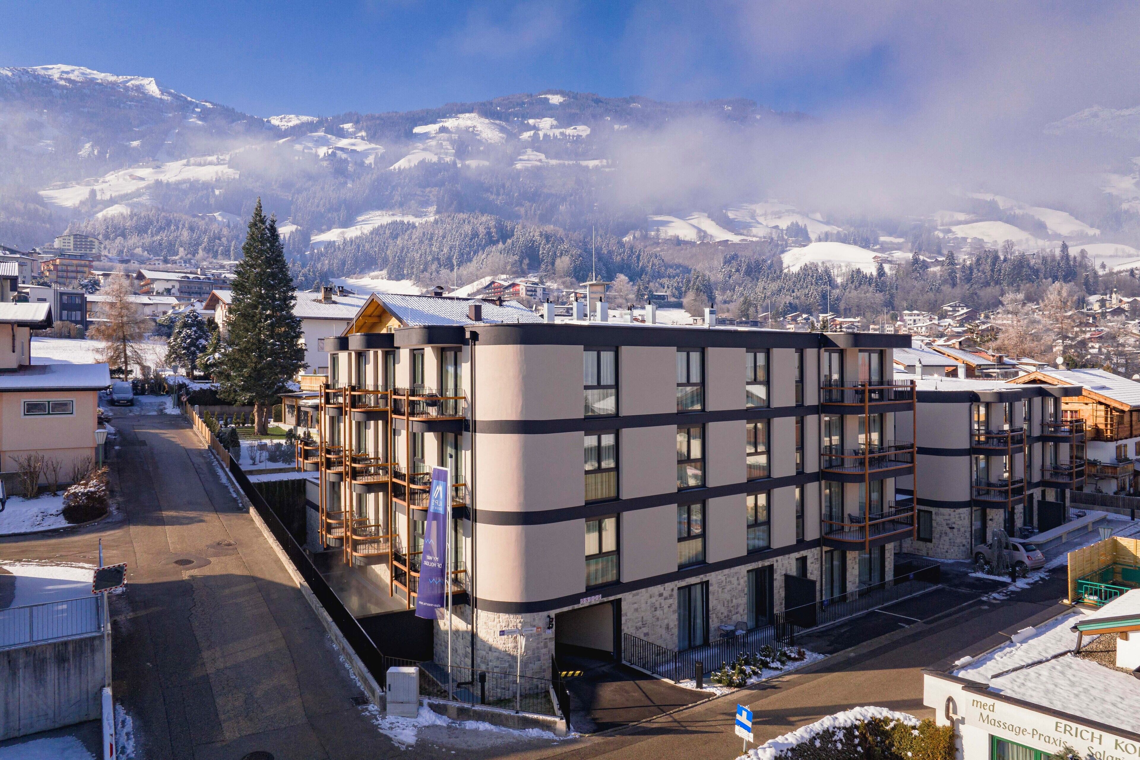 A modern building with a multi-story structure, a parking area, and a view of snow-covered mountains in the background.